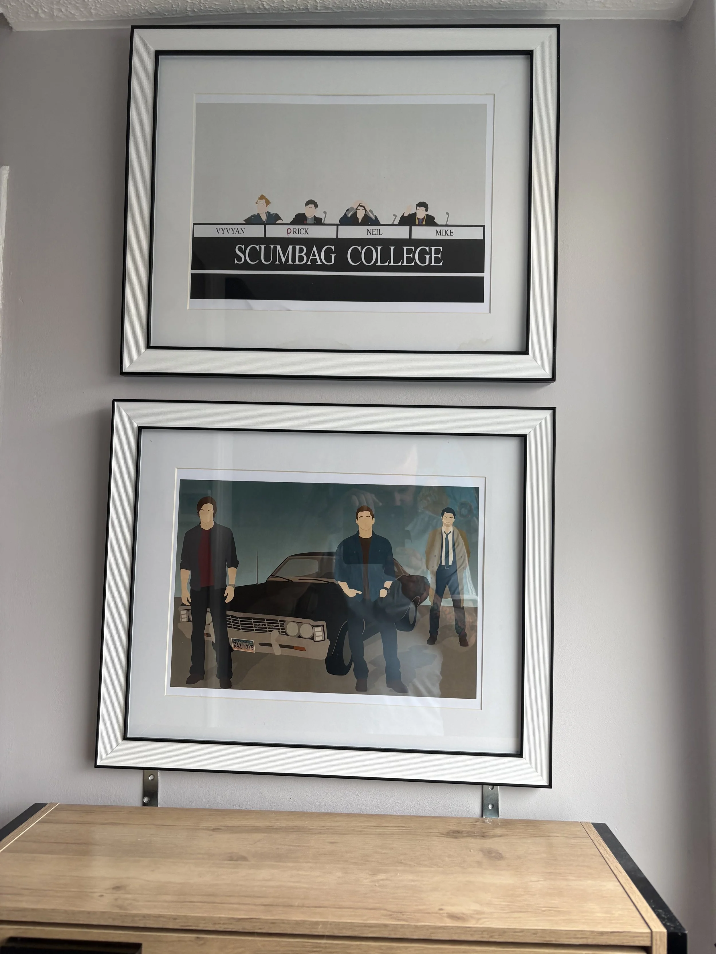 Framed artwork hanging on the wall, depicting animated characters from the TV show 'Scooby-Doo'. The characters are standing in front of a black car, with one character in a brown jacket and two in similar casual attire.