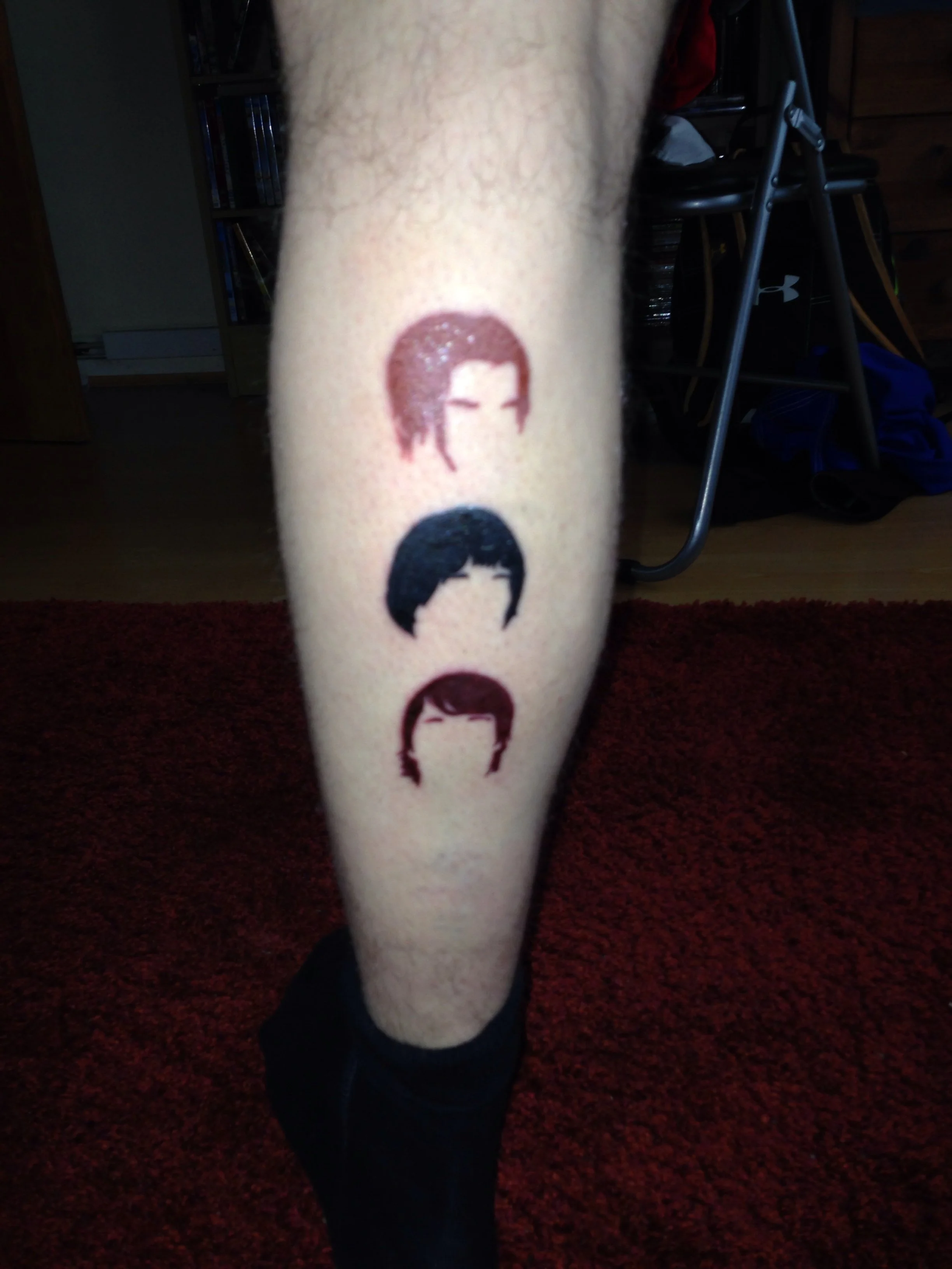 Tattoo of four stylized portraits of people's faces on a person's leg, each with different hairstyles and hair colors.