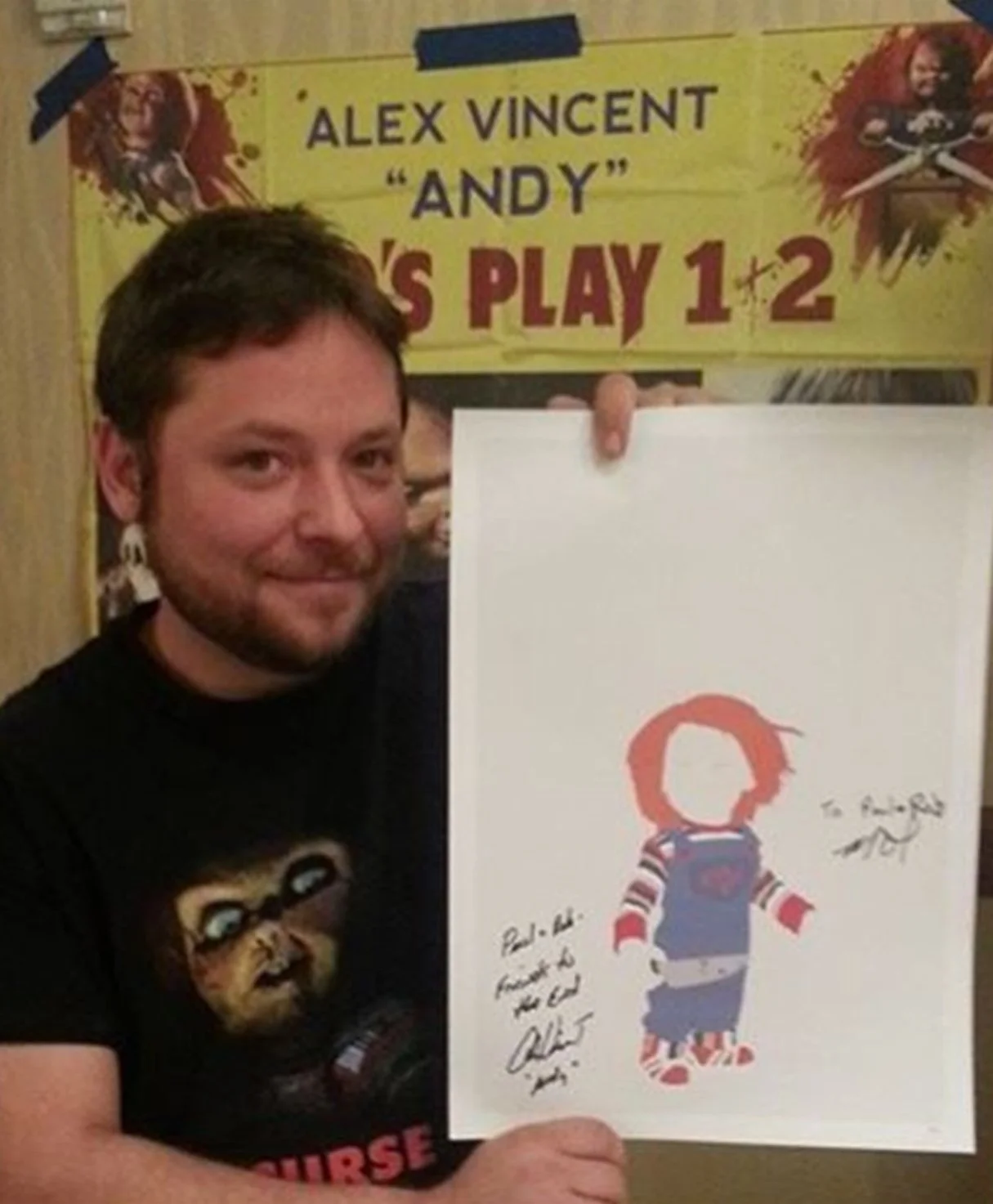 A man holding an art print of a child with red hair, wearing a striped shirt, overalls, and sneakers, with signatures and messages. In the background, there is a yellow banner for Alex Vincent and the movie 'Child's Play 1 & 2'.