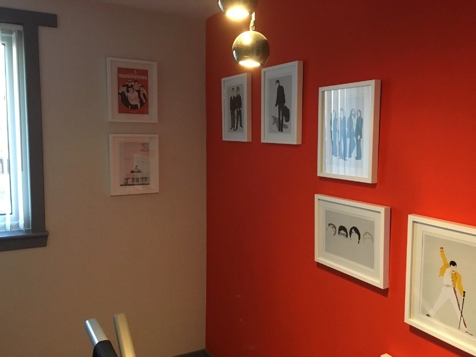 Gallery wall with framed posters and illustrations, one featuring text about 'transporting' on a red accent wall, with a window and part of a chair visible.