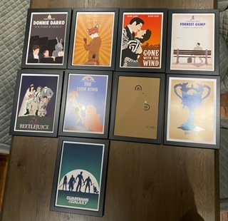 A collection of ten framed posters or book covers arranged on a wall and one on a table, featuring various titles and artwork.