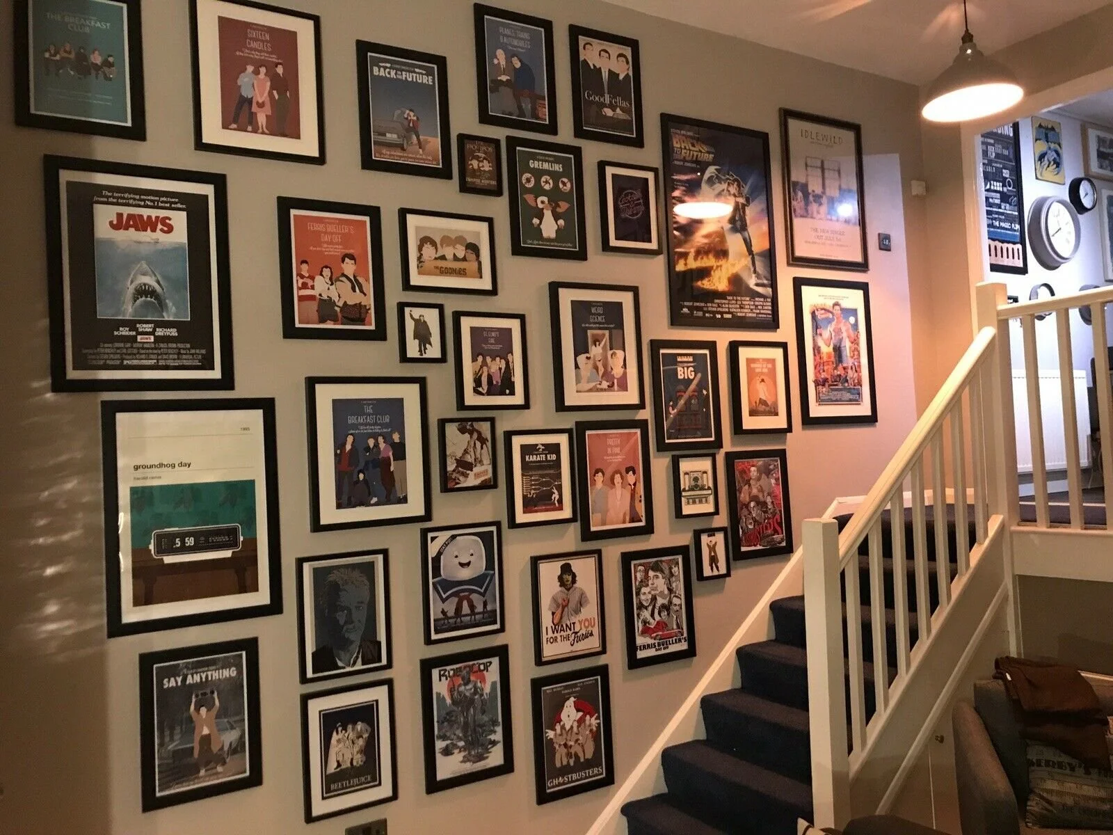 A staircase next to a wall decorated with framed movie posters and artwork, with a ceiling light overhead.
