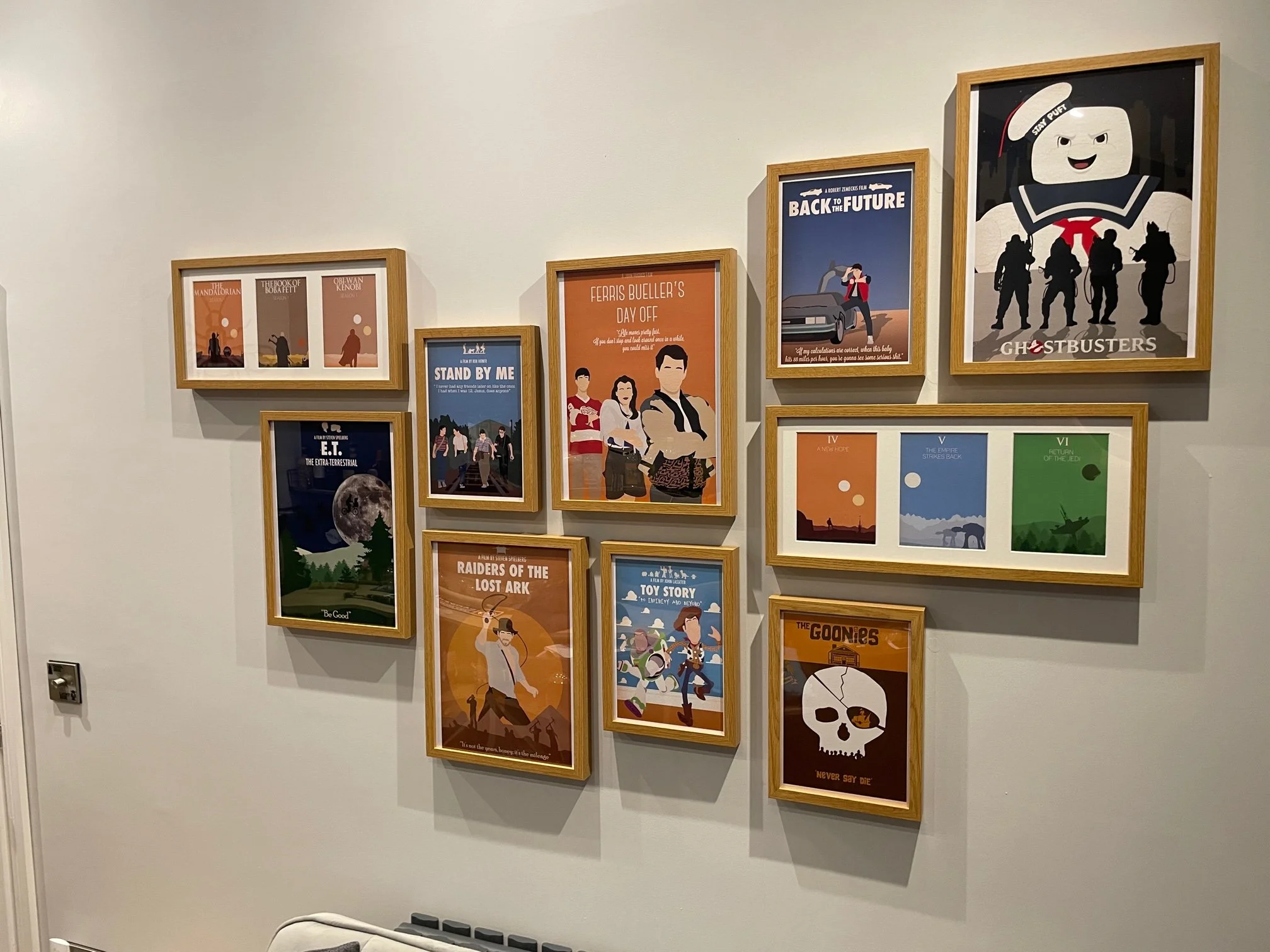 Collection of framed posters on a white wall, including titles like 'Back to the Future,' 'Ghostbusters,' and various movies and animated characters.