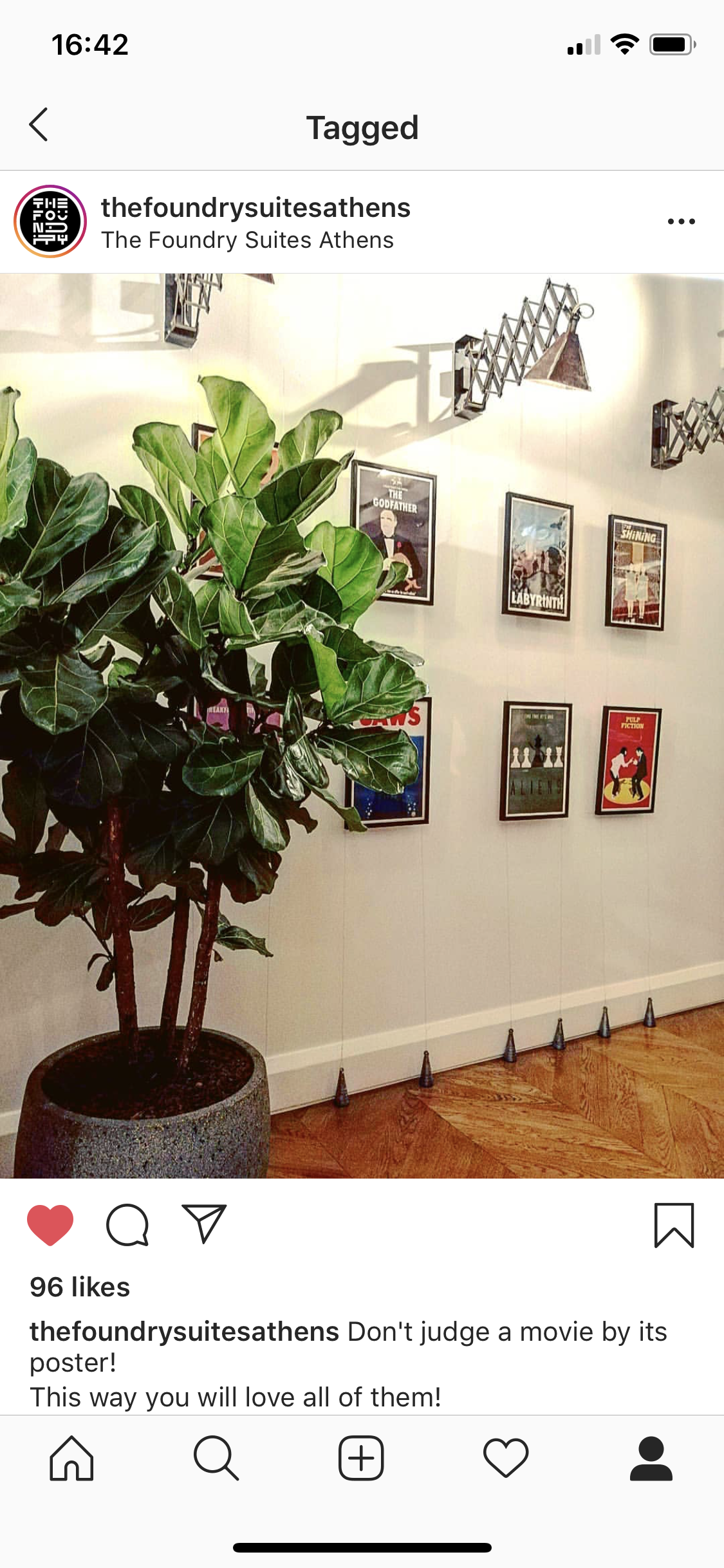 A potted green plant with large leaves is in front of a white wall decorated with framed movie posters. A unique retractable wall lamp extends from the wall.