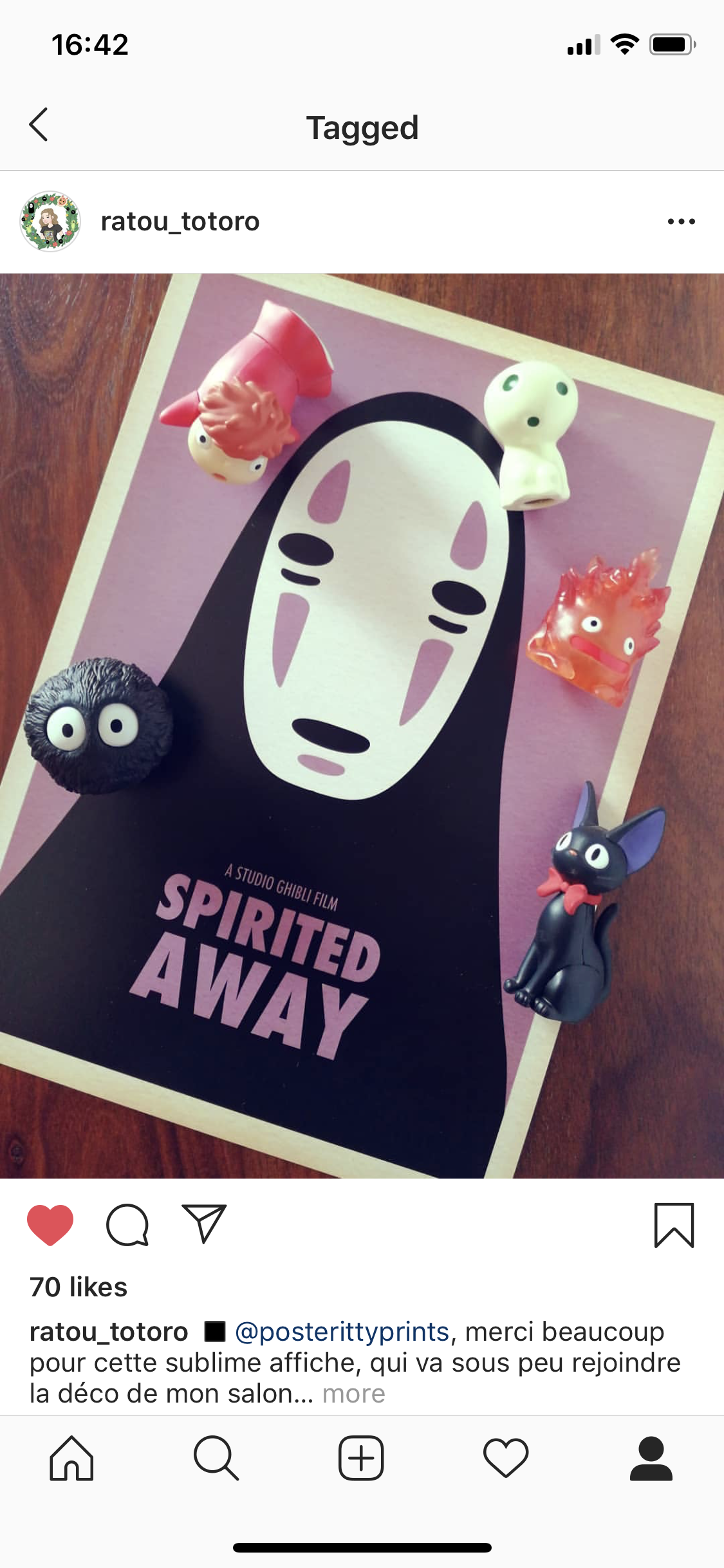 Image of a poster for the film Spirited Away with four small figurines placed around it, including a soot sprite, a white ghost-like creature, a pink creature, and a black cat with a red bow.
