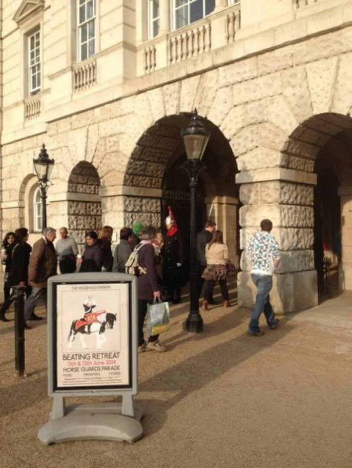 A group of people standing in line outside a building with large stone arches and lantern-style streetlights.