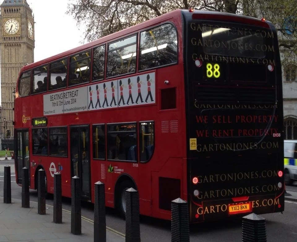 Red double-decker bus on a city street with an advertisement for a retreat and a sign for bus route 88.
