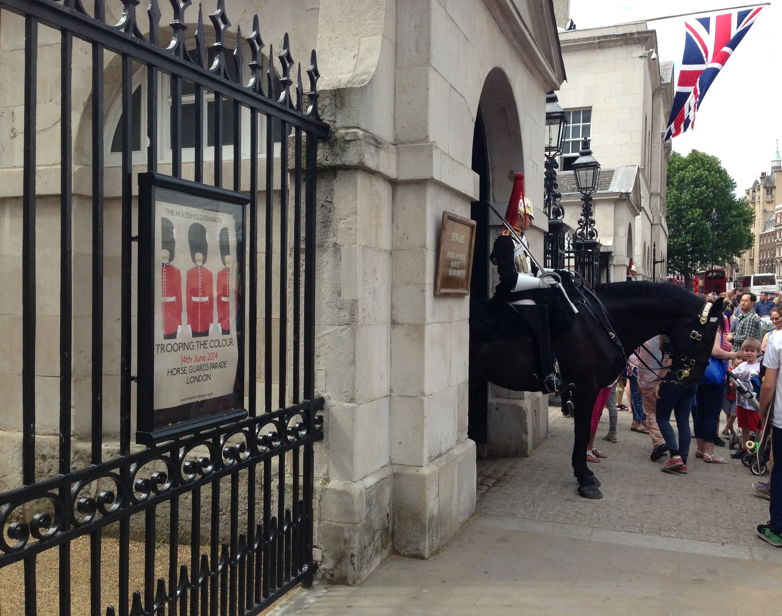 A street scene in London, England, with a horse-drawn carriage, people walking, and a Union Jack flag hanging outside a building.