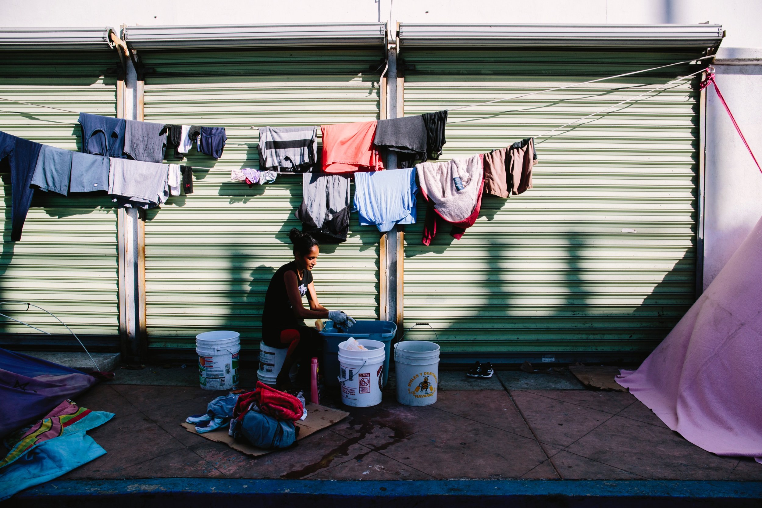  A woman washes and hangs laundry to dry in el Chaparral migrant camp. Tijuana, Mexico. June 2021. 
