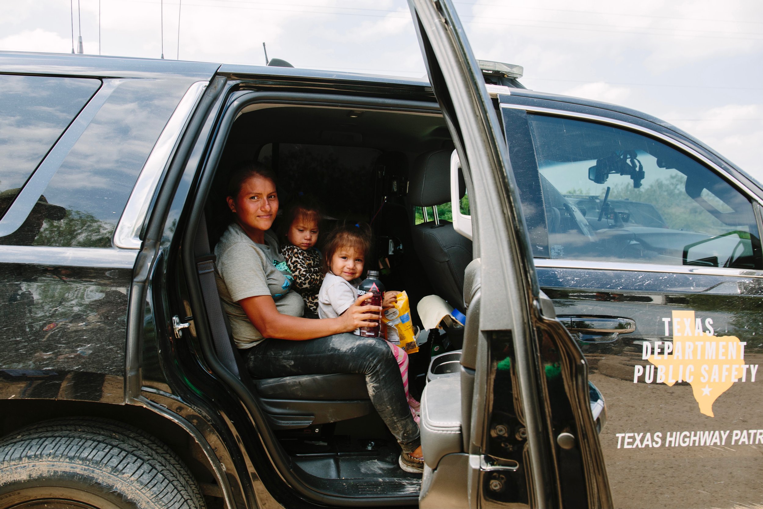  A mother with her twin girls cool off, in a Texas Highway Patrol vehicle, after crossing into the United States, from Mexico. La Joya, Texas. USA. June 2021. 
