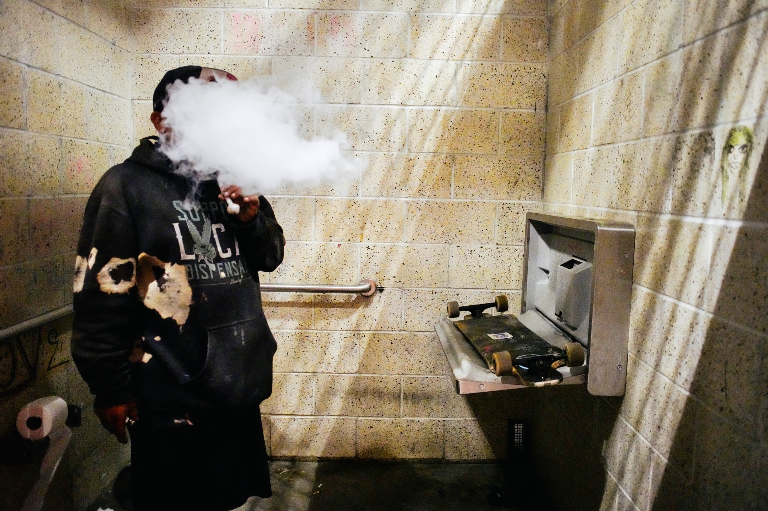   A man smokes crystal meth in the public beach bathrooms. January 2022. Venice Beach, Los Angeles, CA.  