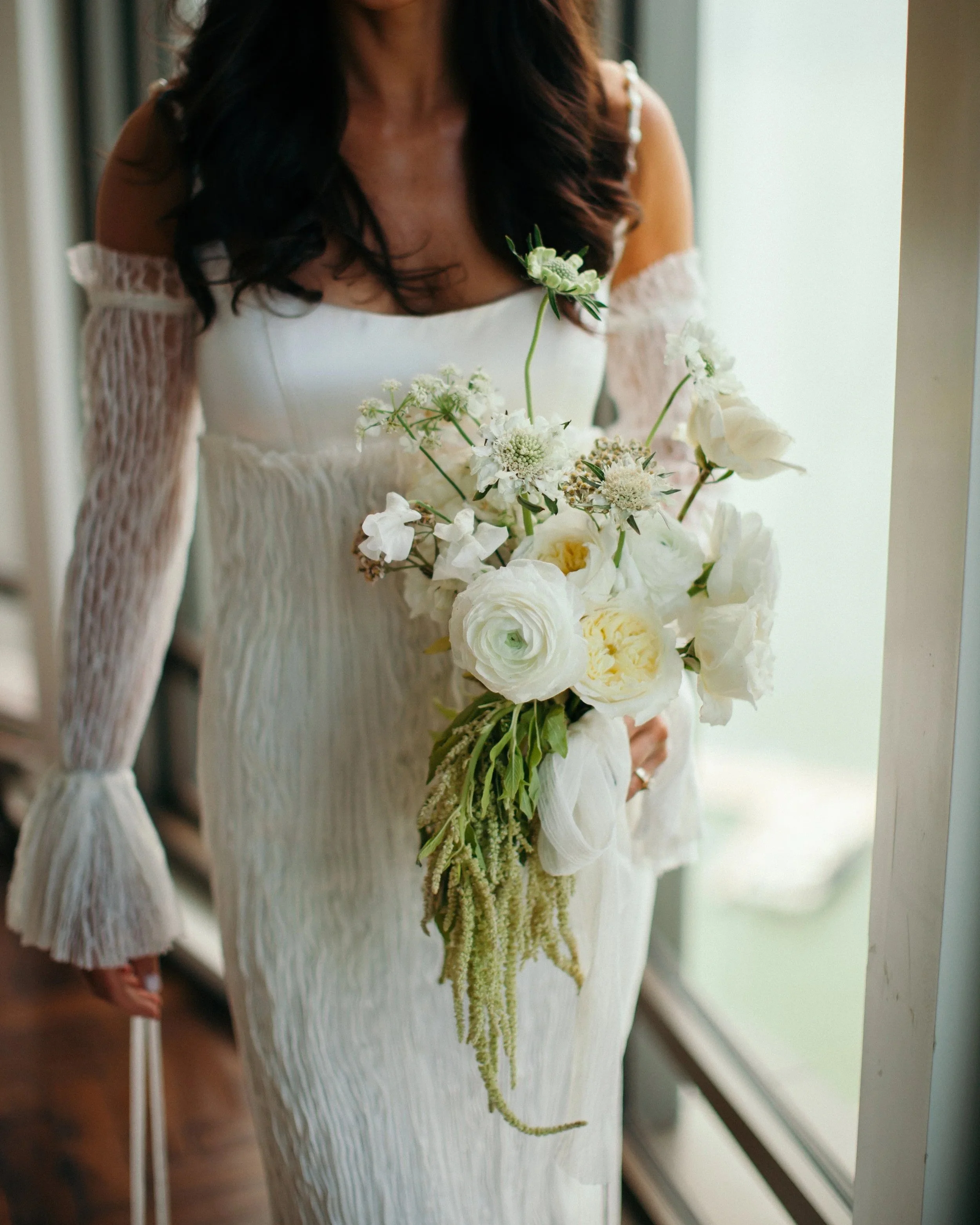 Bride holding a modern white bridal bouquet with ranunculus and airy florals at The Edgewater Hotel wedding in Madison, Wisconsin, designed by 1209 Creative.
