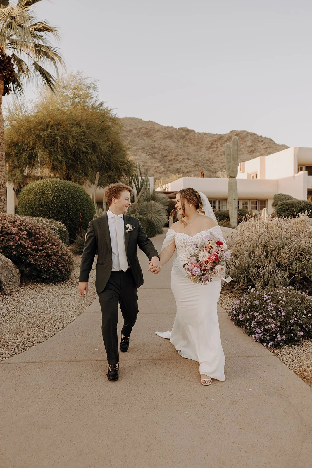 Bride and groom walking together at a Camelback Inn wedding in Phoenix Arizona with florals designed by 1209 Creative, set against a desert landscape and mountain views