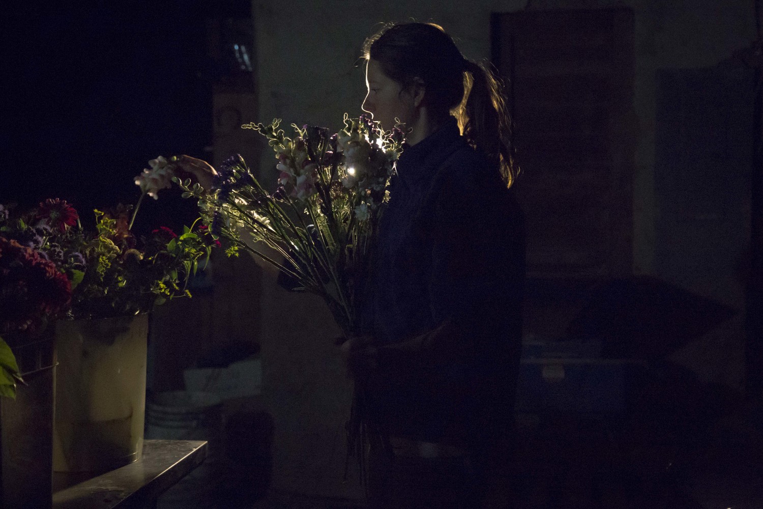 Flower farmer Claire working in the middle of the night making bouquets for a wedding after a day of harvesting on the farm. (British Columbia)