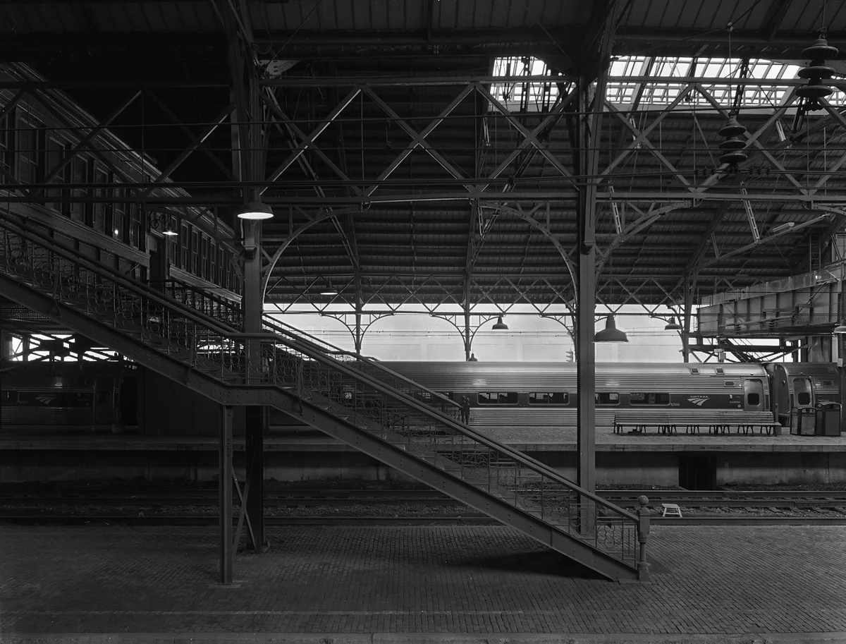 Train shed interior looking east. Notice the intricate iron work on the stair railings and trusses. The active center platform has been elevated to accommodate Amtrak/ ADA compliance needs but the remaining low level platforms are still traditional herringbone brick with stone curbs. This shed is one of few remaining examples of a style of station that was once commonplace in America.