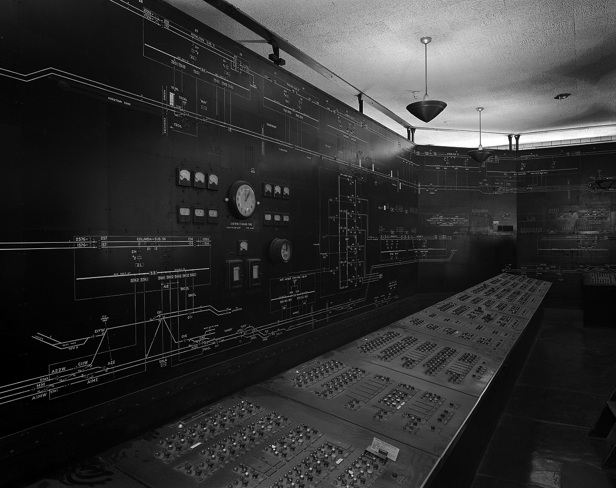 Panel detail of Power Dispatcher's Office in the Harrisburg Passenger Station. This impressive installation dates back to the 1937 electrification to Harrisburg and was responsible for monitoring and controlling electrical loads and supply from Thorndale and Perryville west to Harrisburg. Along the three walls the entire mainline system is illustrated noting substation installations and interlockings, accompanied by indicator lights for the status of both train and signal power. In the foreground are control panels that correspond and essentially functions as breakers for all circuits, phase breaks, and sub stations. This would be a stressful place to work during inclement weather as dispatchers worked against ice, lightning and heavy winds to maintain power to keep trains moving in adverse conditions.