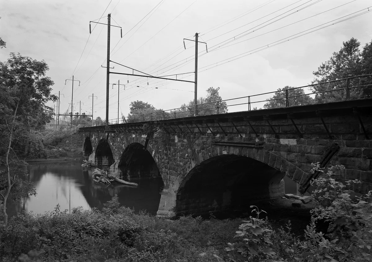 A four arch stone bridge of Chief Engineer William H. Brown's design carries the mainline and Royalton branch over the Swatara Creek. In the distance is the home signals for Roy interlocking which marks the point where freight would diverge off the mainline south to Columbia.