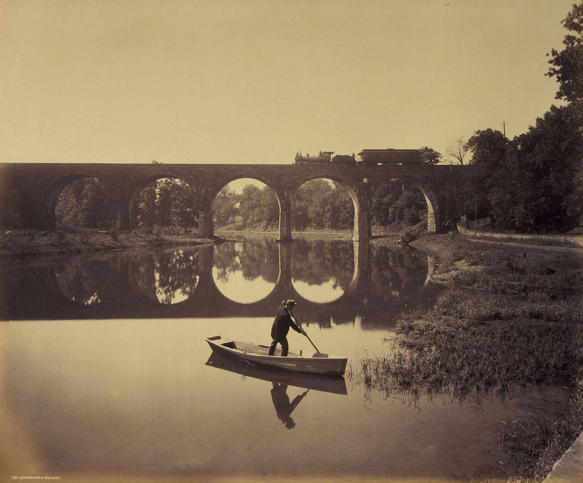 In a beautiful image by William H. Rau we see the Conestoga River bridge, one of Brown's first stone bridges. Utilizing the figure and boat as a device for scale in the foreground Rau is looking south, as noted by the finished facade of the bridge. To the left out of view is the Lancaster Water Works which still survives today. Photograph collection American Premier Underwriters, Inc. 