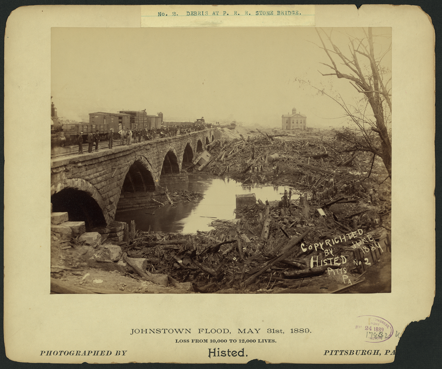 The great stone bridge on the Pennsylvania Railroad's main line played a large role in the devastation during the flood when debris washed across the valley piling up against the bridge creating an unintended dam, trapping flood victims in a 70' high debris pile that burned for three days. After the fire and flood water subsided clearing of the bridge required the expertise of "Dynamite Bill" Flynn and a 900 man crewtaking 3 months to complete the task. Photograph by Ernest Walter Histed, collection of the Library of Congress.