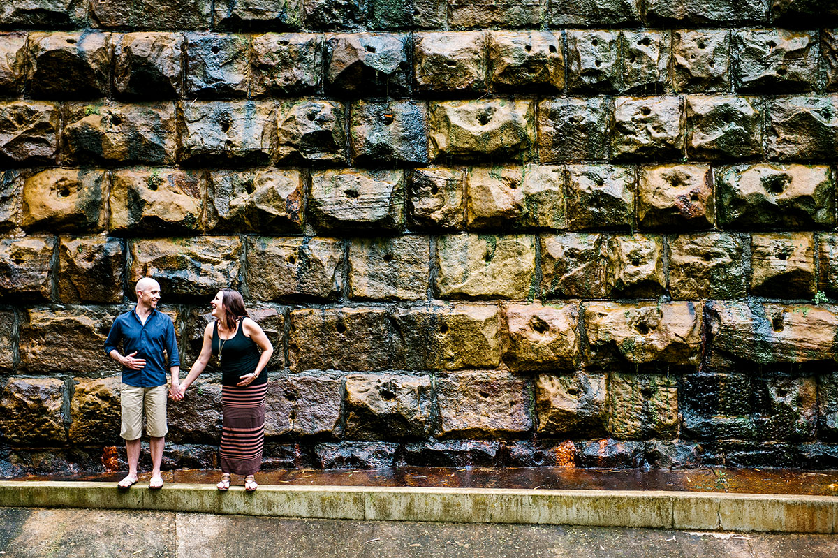 Pregnant couple laughing in front of textured stone wall