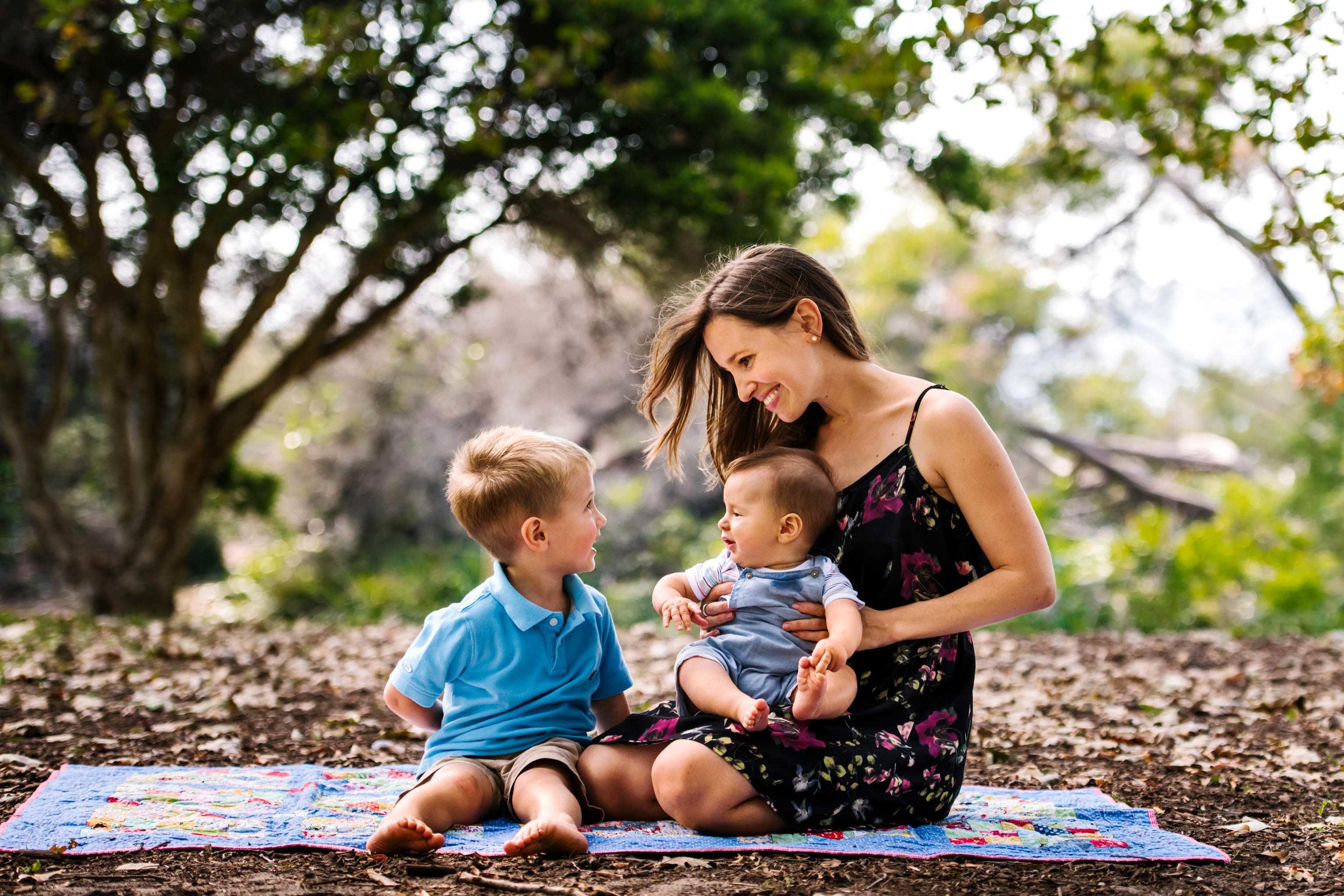 Mum looks at older son while holding a cute baby on her lap