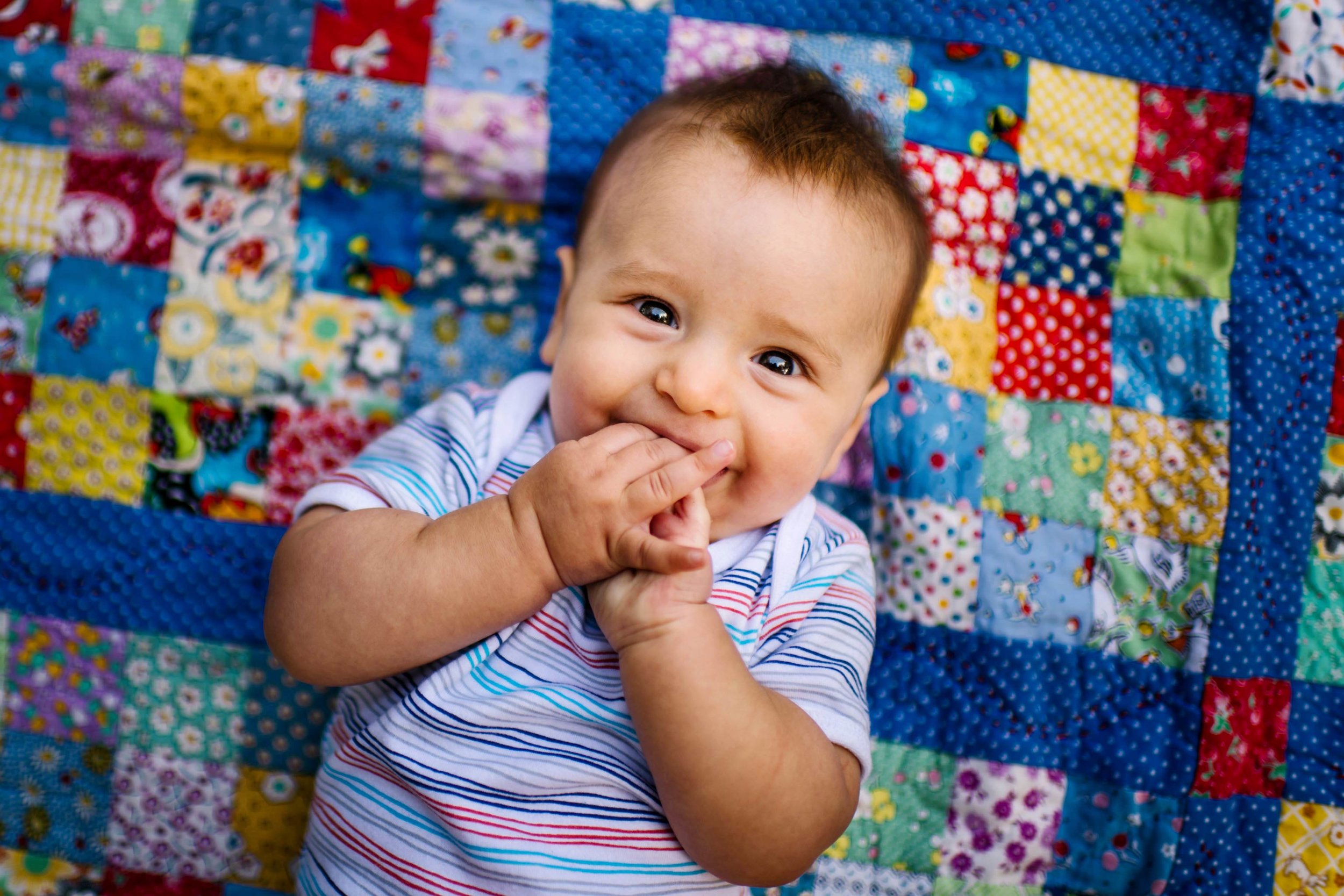 Baby boy smiling while lying on patchwork blanket