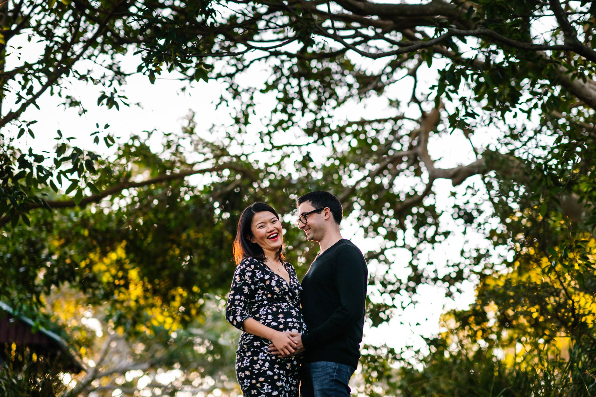 Pregnant couple laughing with trees in the background