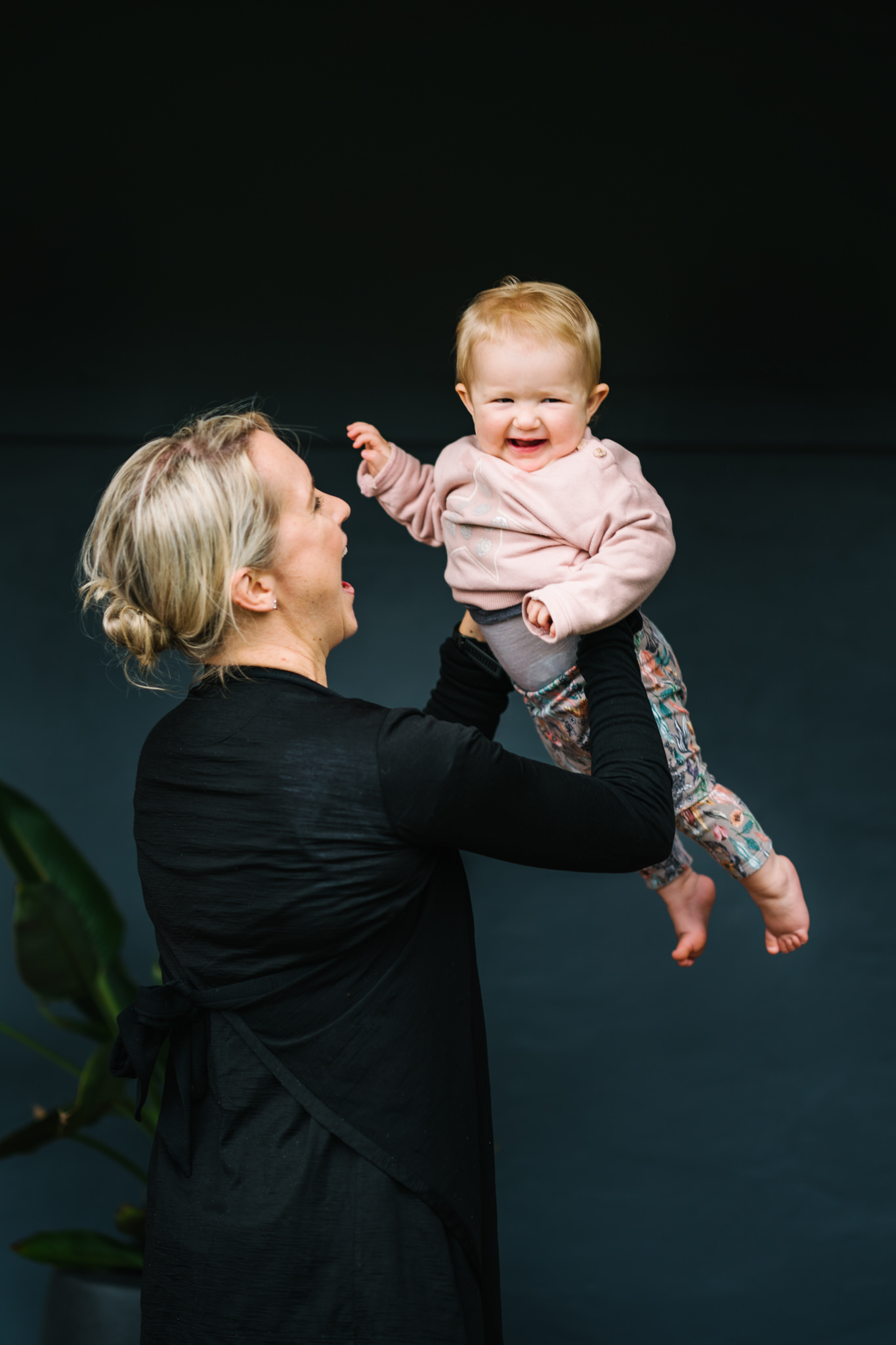 Baby girl smiling at camera as her mum holds her up in the air