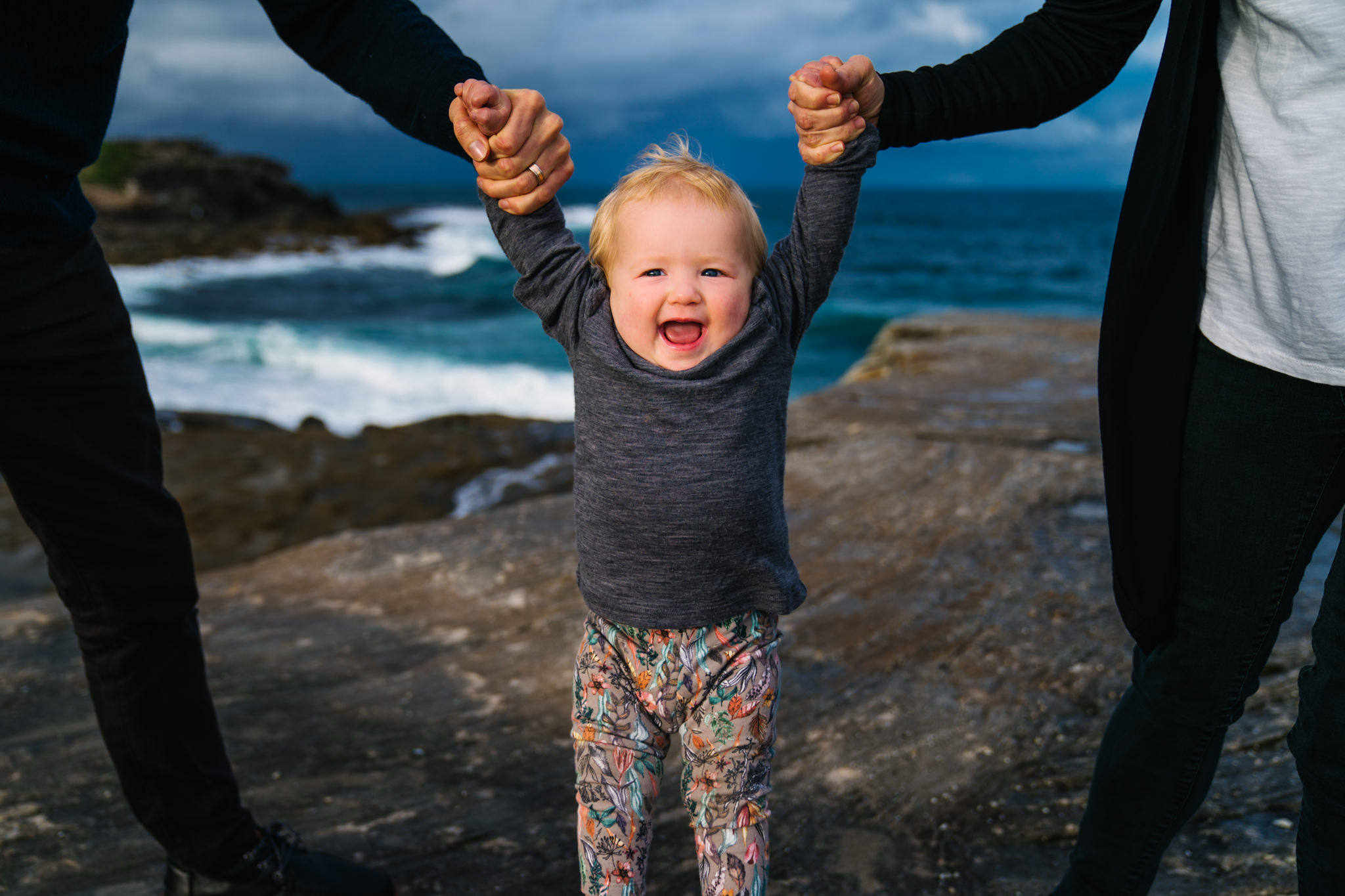 One year old girl laughing as she is held between her parents during family photography session