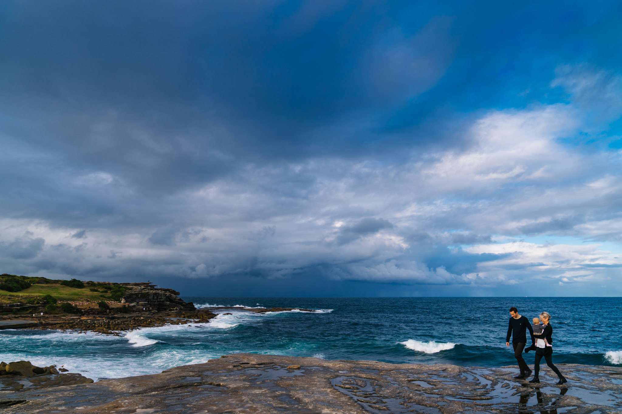 Stormy skies over Coogee beach as family walks along the rocks