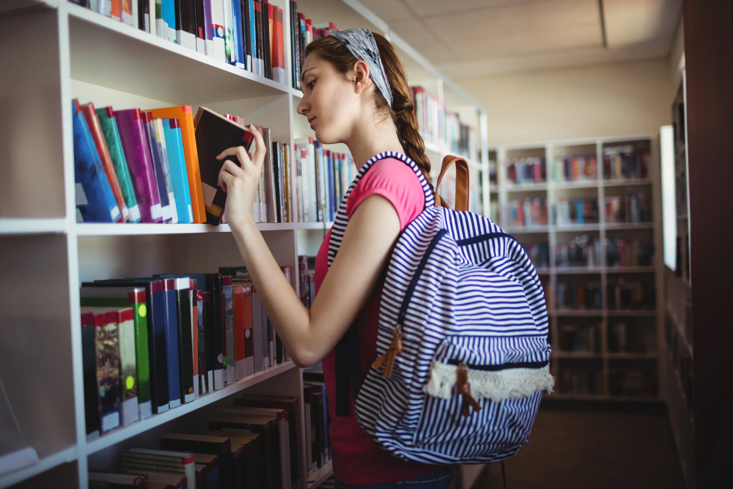 schoolgirl-selecting-book-in-library-HRBTC5F.jpg