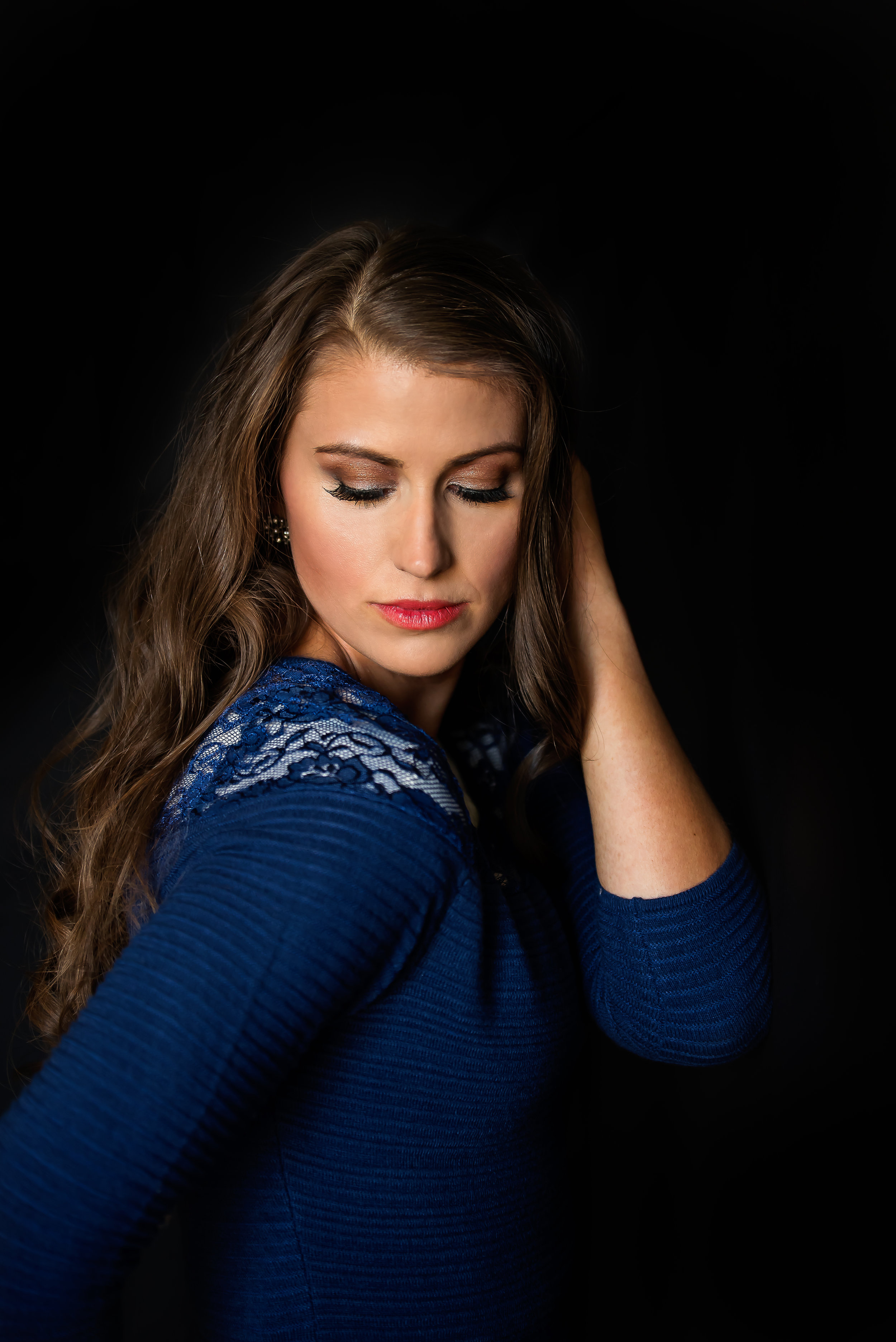  Black background with woman in blue sweater looking down over her shoulder. 