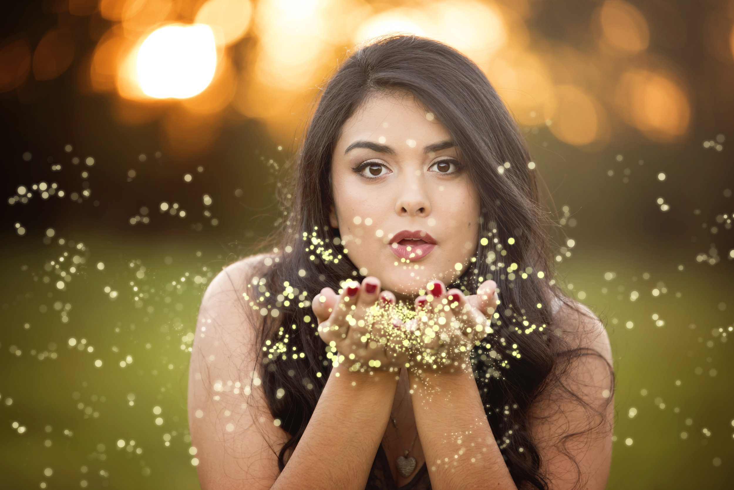  Portrait with light from sunset in the background, woman blowing on dandelions cupped in her hands.  