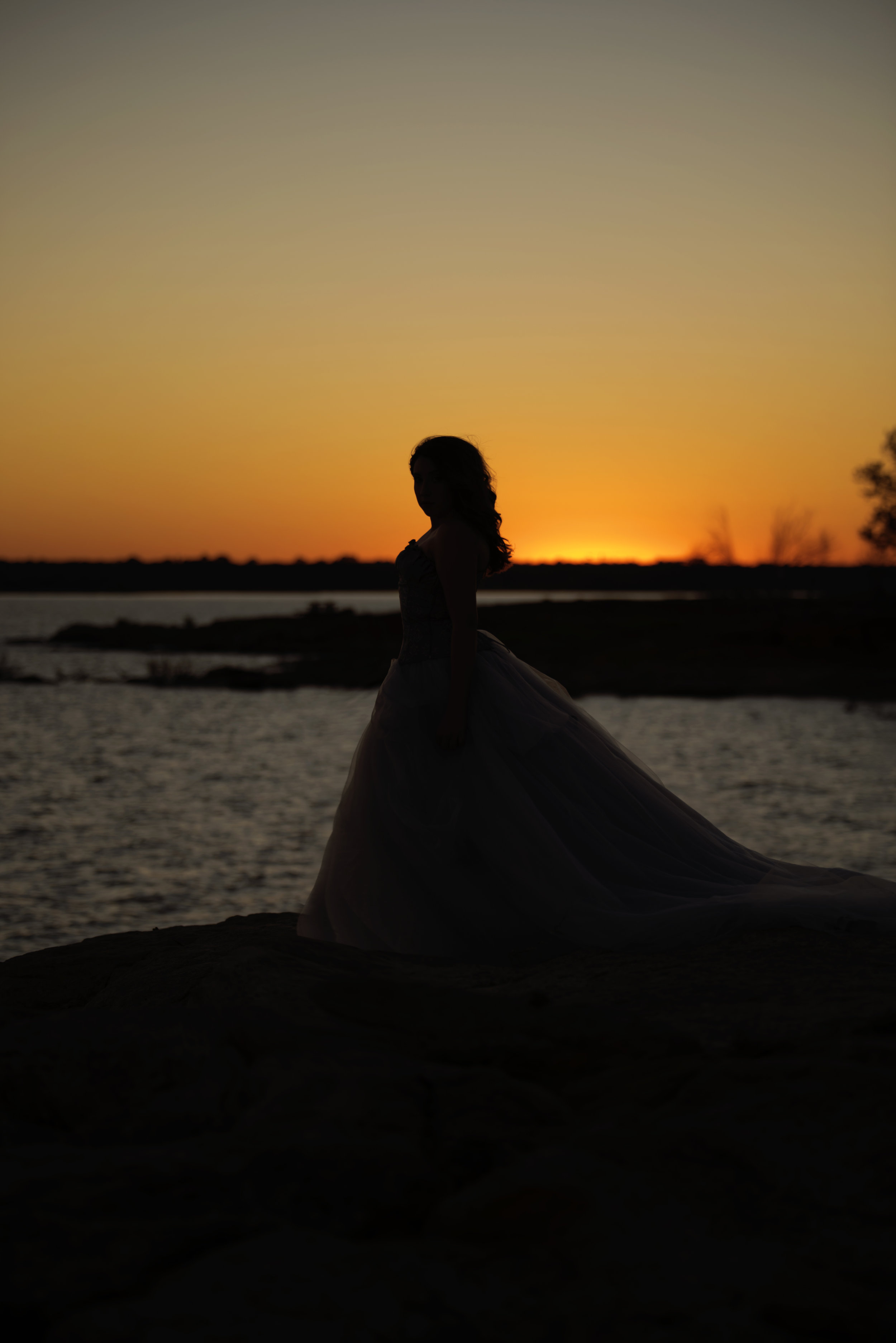  Silhouette of a woman in a dress at dusk, with the sun in the background. Castle Rock  