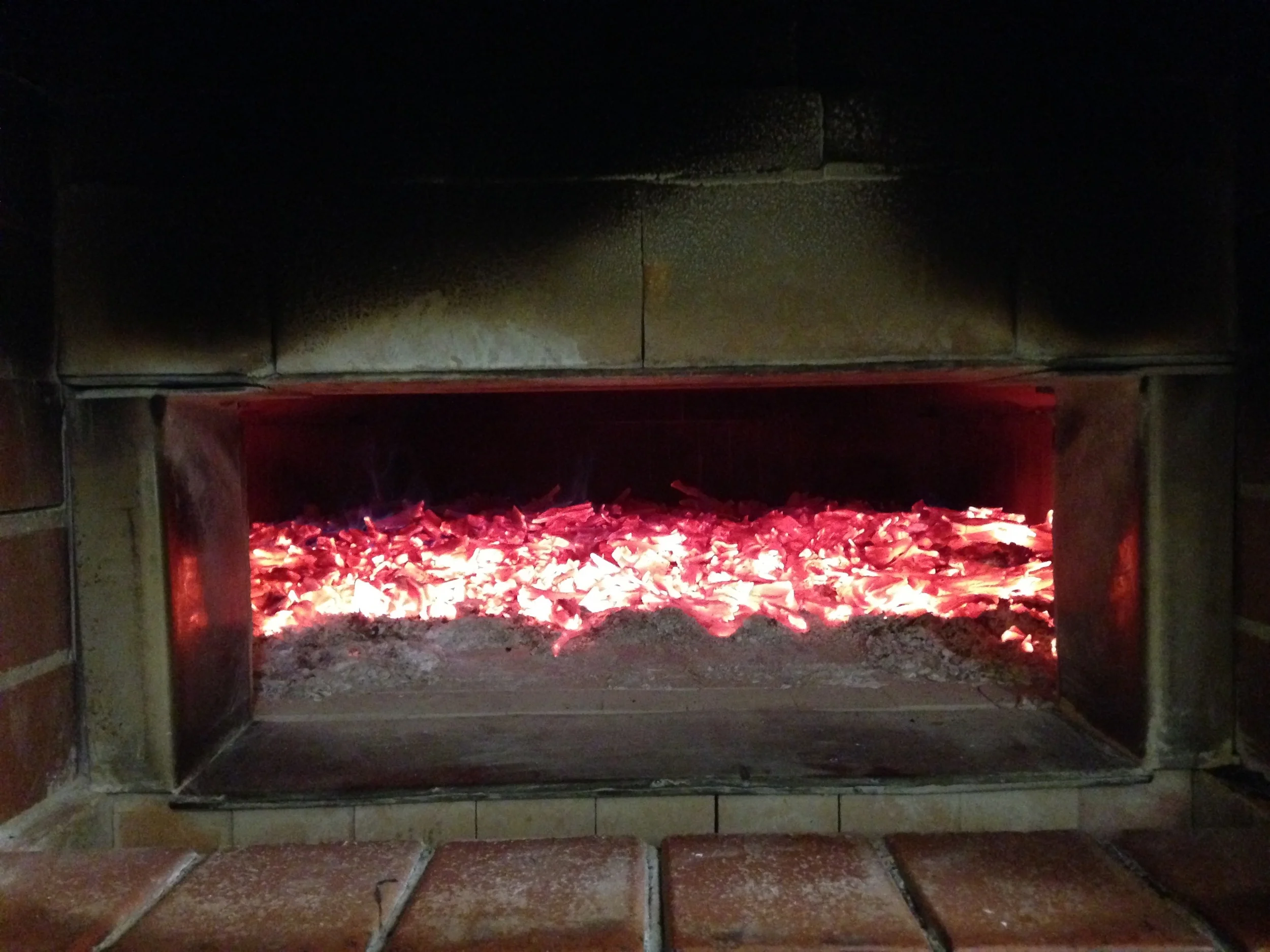 By the next morning the fire has burnt down to a bed of coals. The oven temperature has gone from 100 degrees to about 450 degrees. This temperature will slowly even out across the oven to about 300 degrees when we bake. The coals will reduce to ash, be swept out and the oven will be mopped out leaving a clean, hot brick hearth.