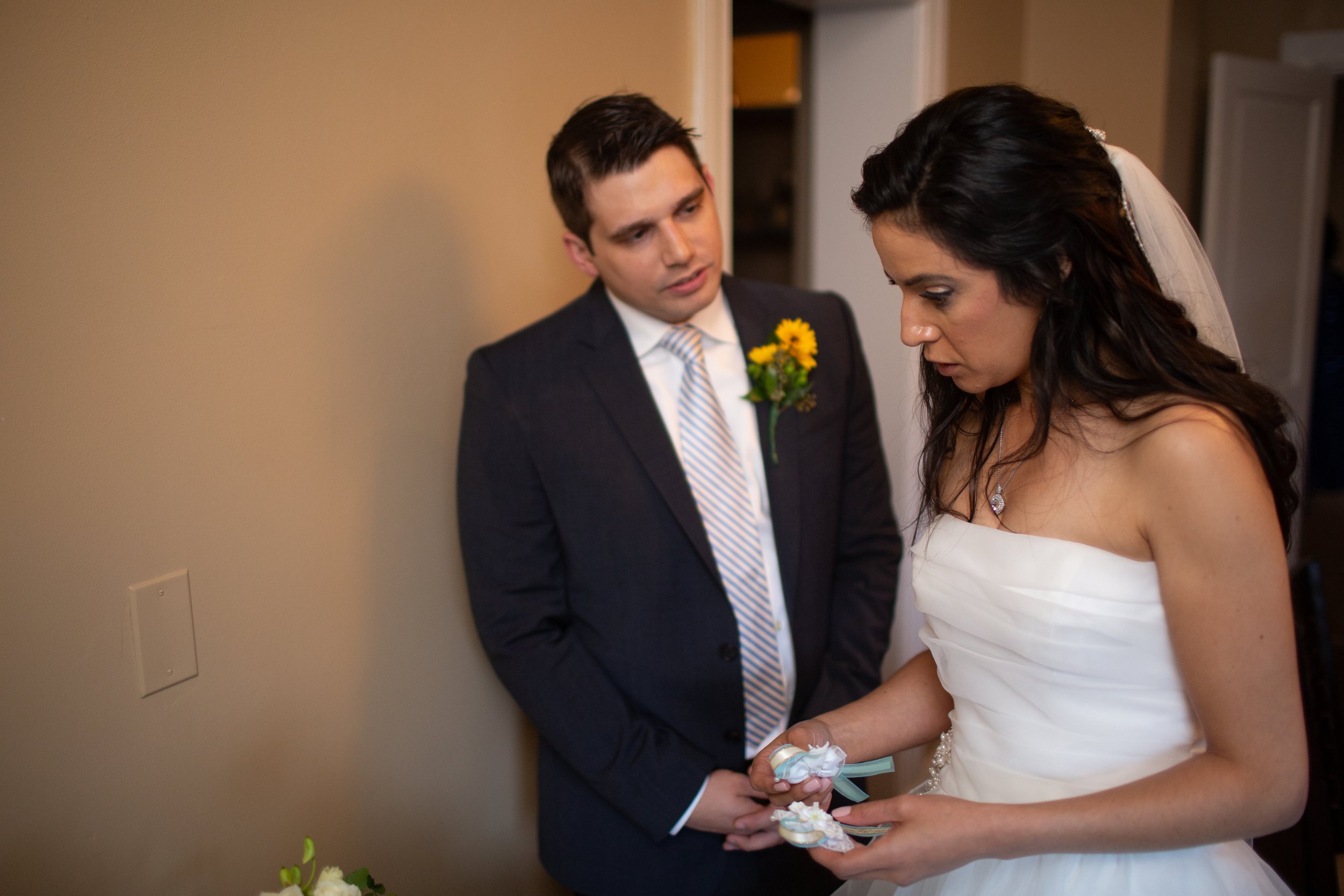 A bride and groom during a wedding ceremony, holding hands and exchanging vows or rings, with the groom wearing a dark suit and striped tie and the bride in a white strapless gown.