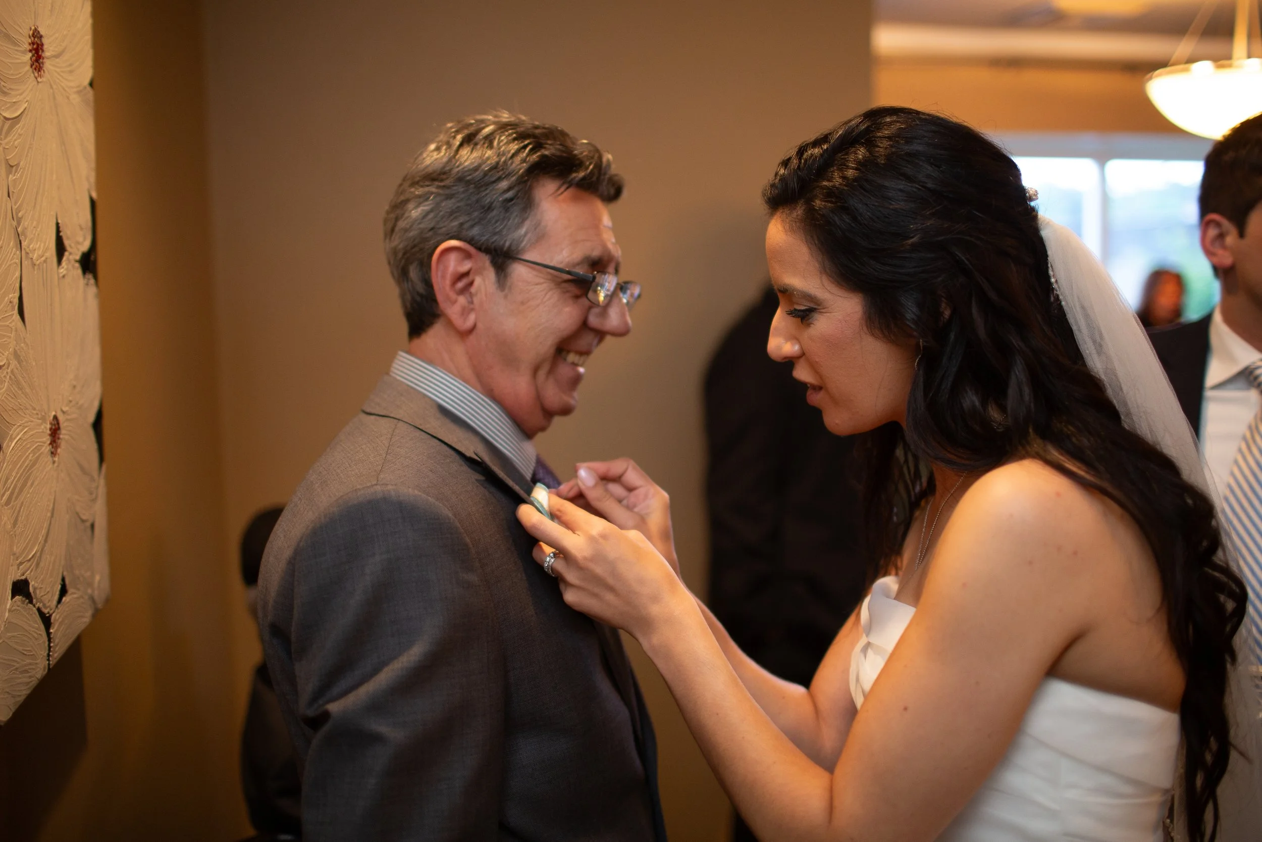 A bride and a groom share a tender moment during their wedding ceremony, with the bride pinning a boutonniere onto the groom's suit.
