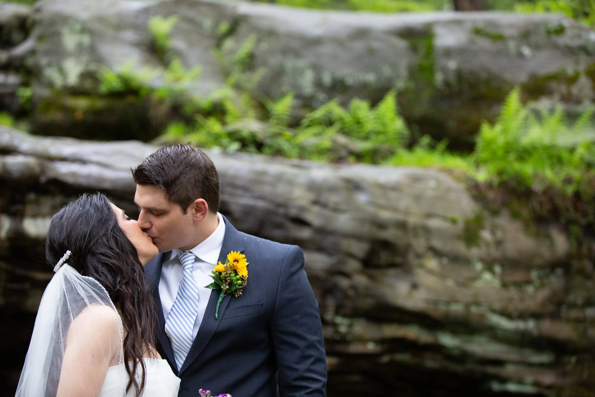 A bride and groom share a kiss outdoors in front of green and gray stone background.