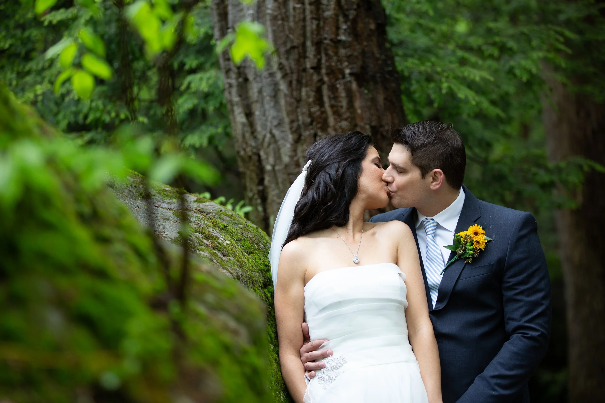 A bride and groom sharing a kiss in a forest setting during their wedding.