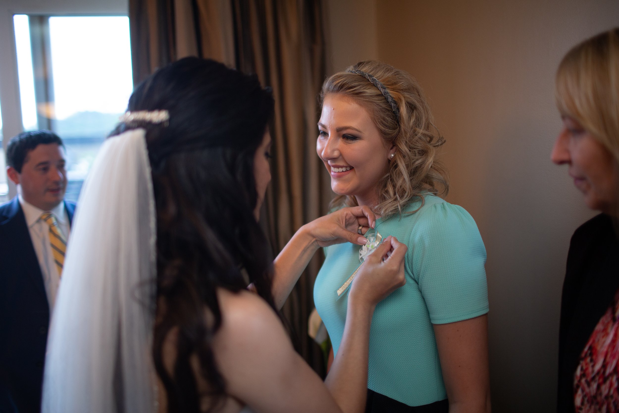 Women in a room, one with a teal shirt smiling as another woman pins a badge on her shirt.