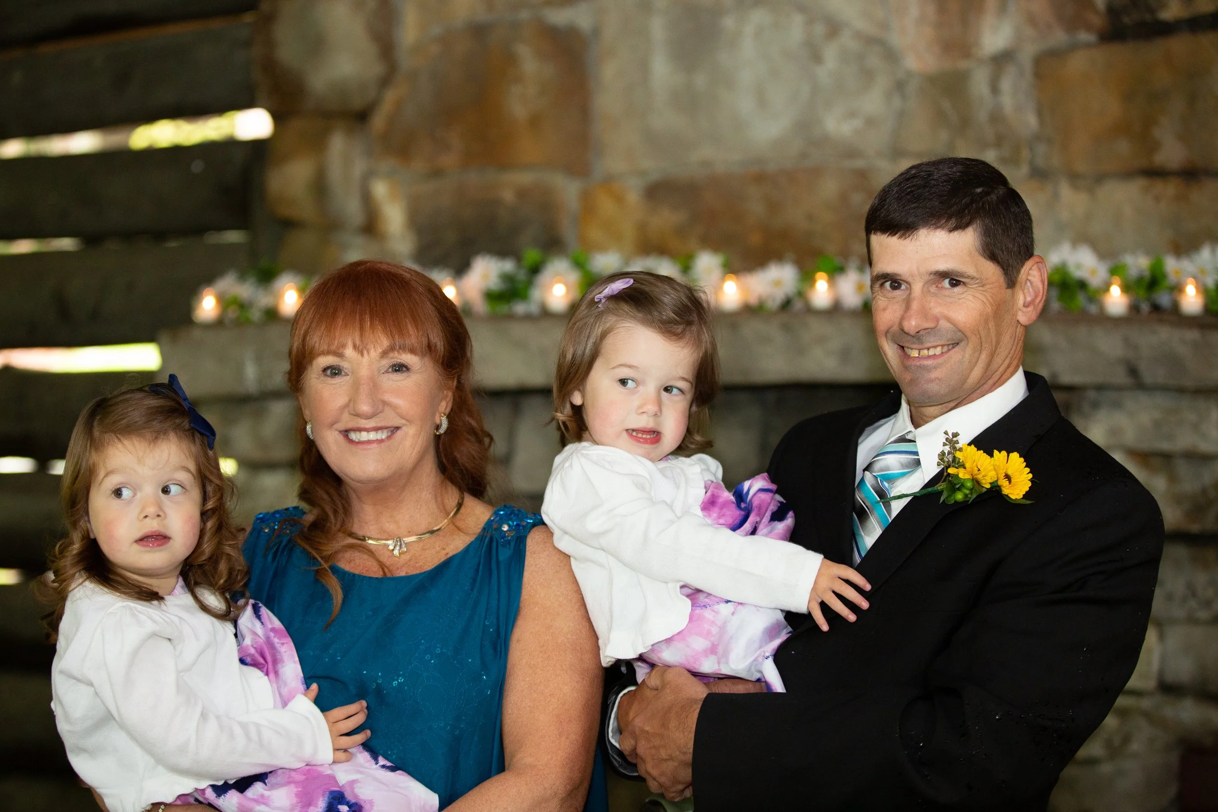 Family scene with grandmother, mother, father, and two young daughters at a celebration, with candles and flowers in the background.