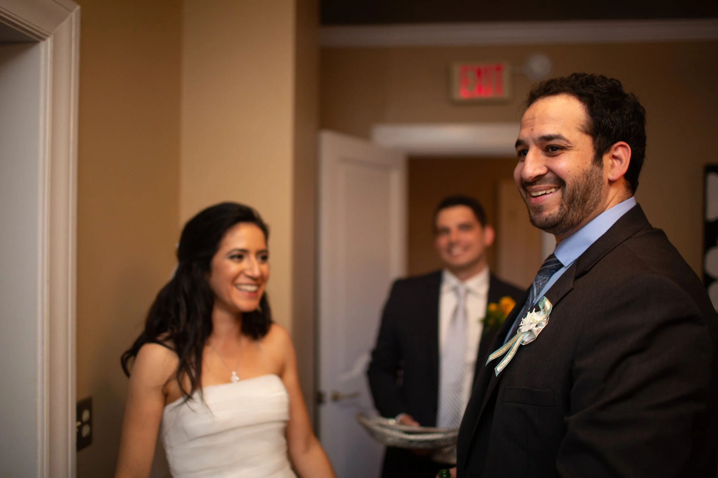 People at a wedding reception, with two men and a woman smiling and talking.