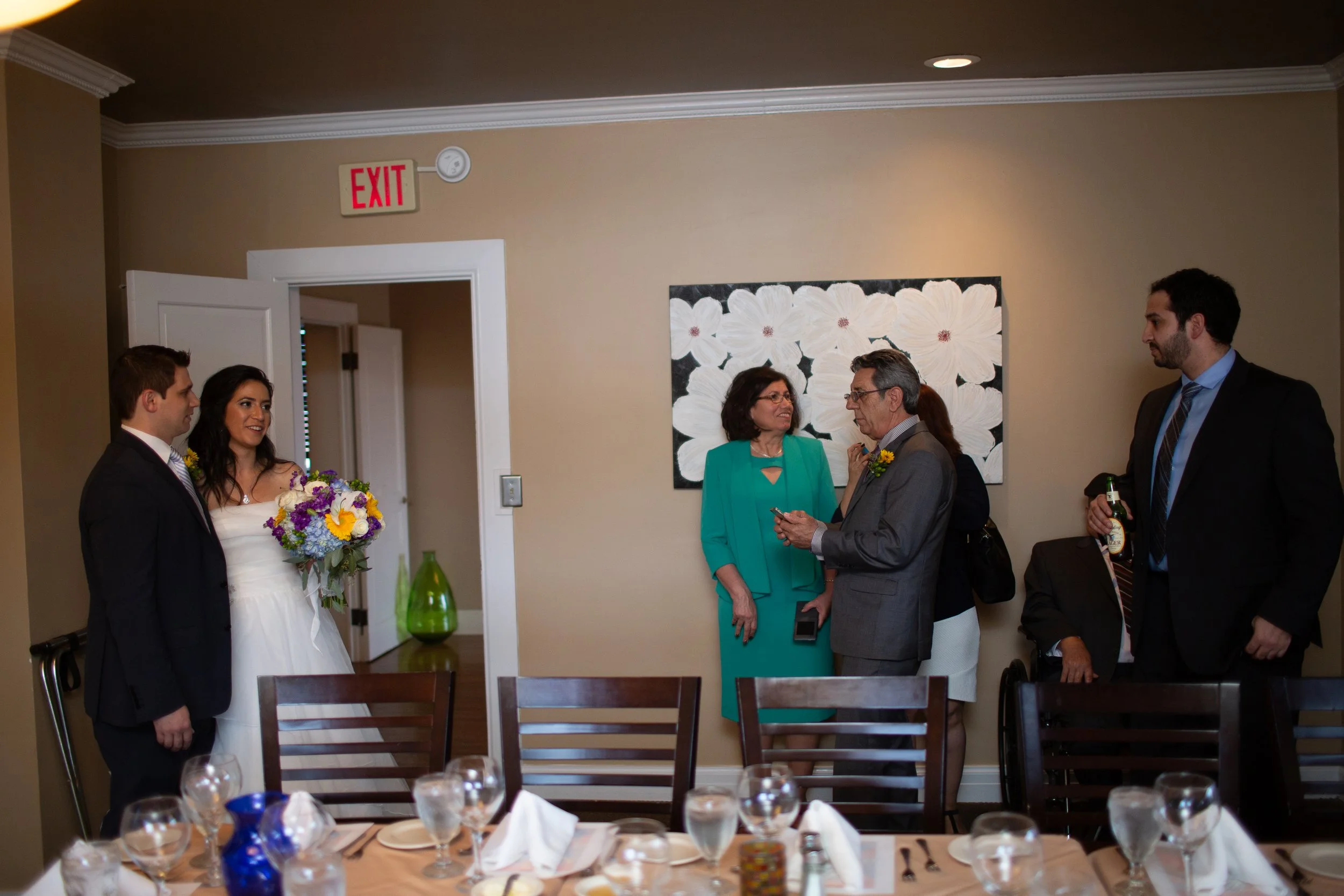 People at a wedding reception talking and smiling, with a dining table set with glasses and napkins in the foreground.