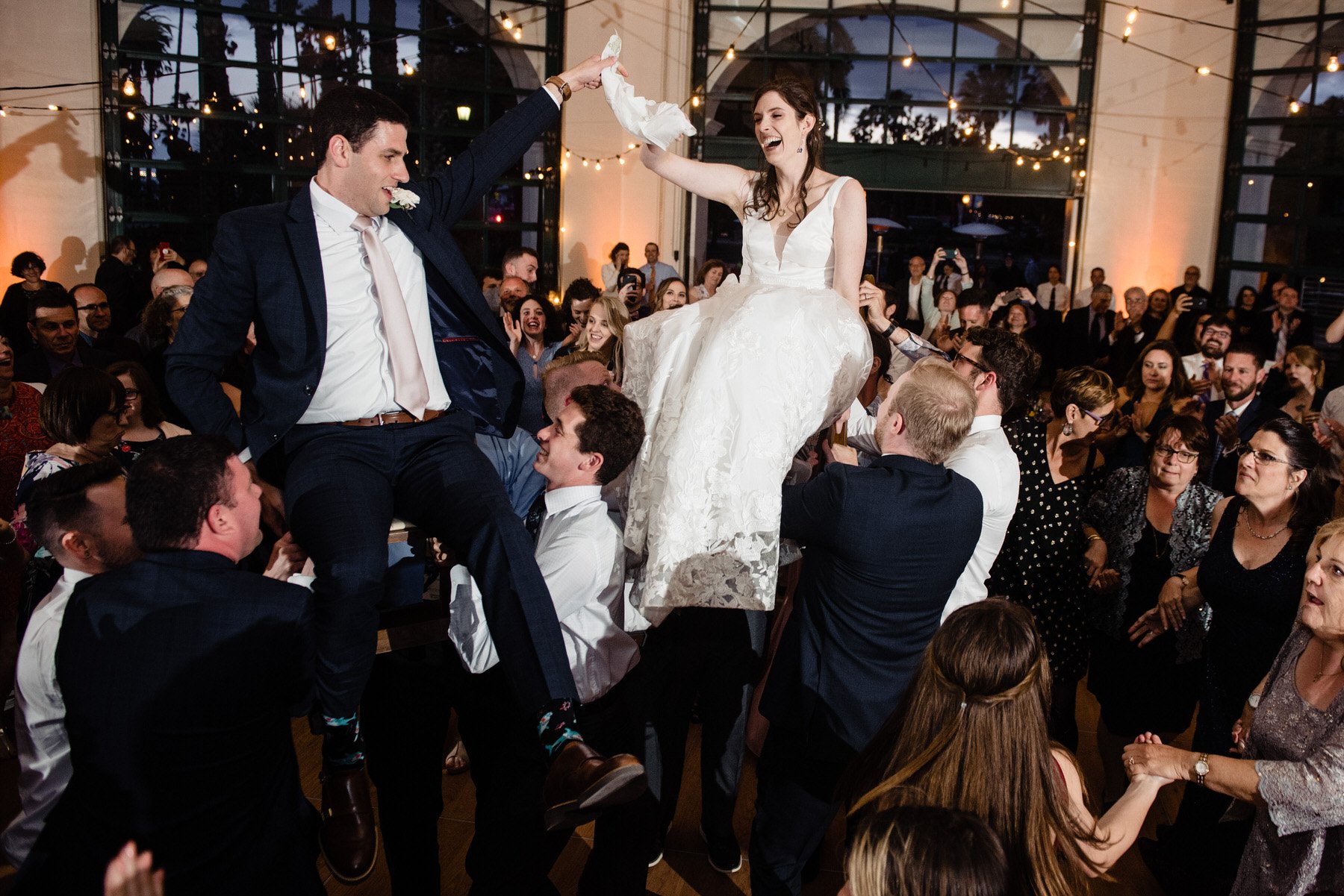 Jewish newlyweds lifted on chairs during a lively hora dance at their wedding reception