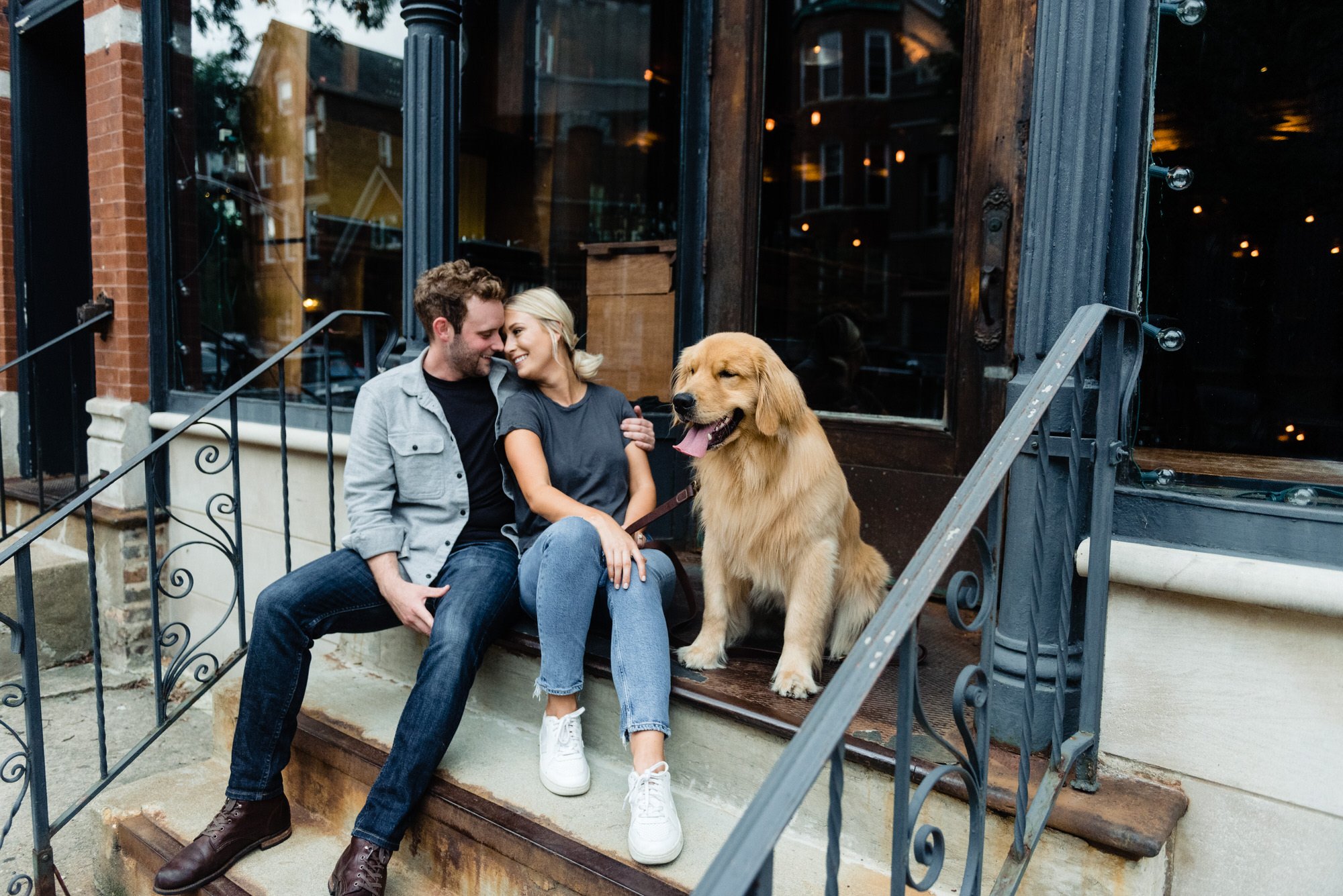 man and woman sit on a porch for their engagement session with a dog