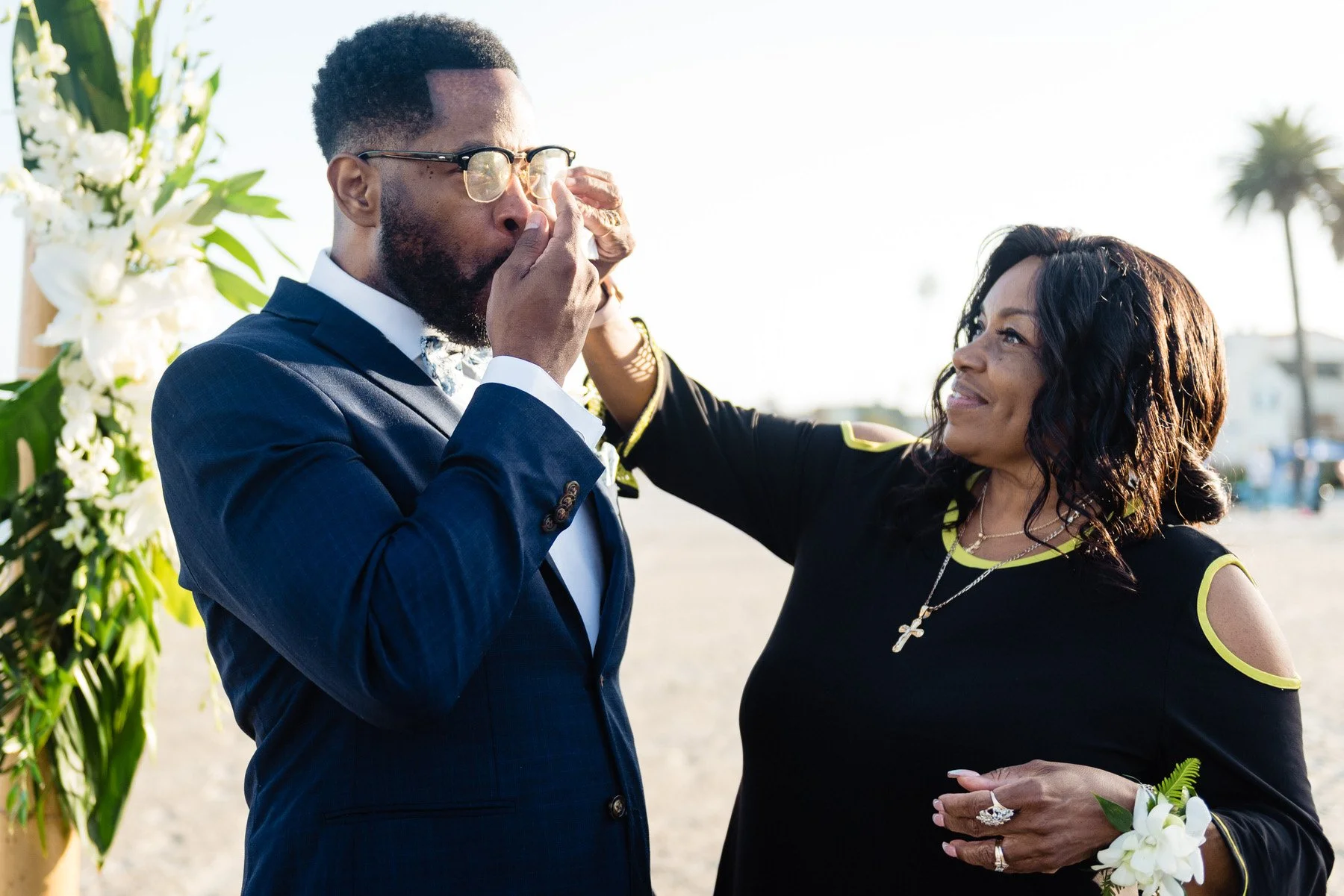 a woman wipes the tears from a groom standing at the front of the aisle