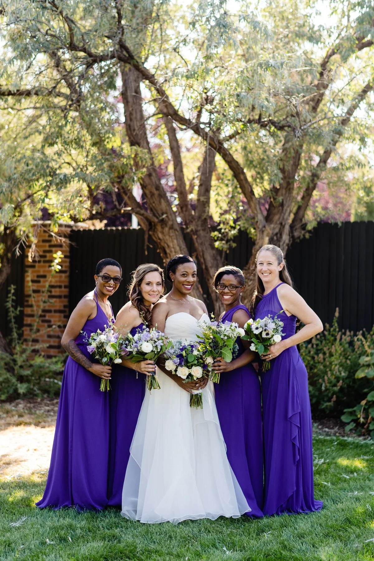 a bride poses with her wedding party in purple dresses