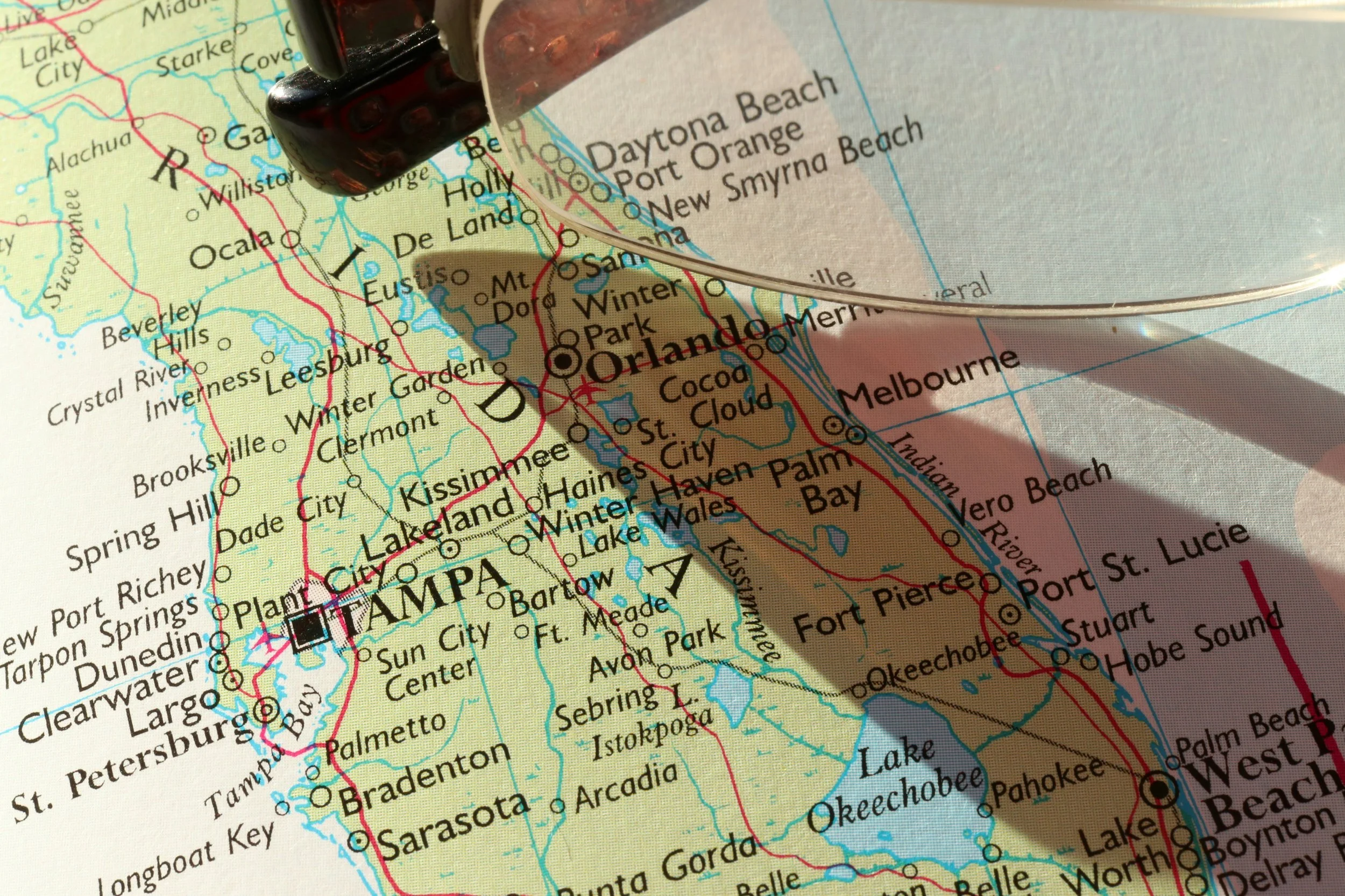 Close-up of a map of Florida with a magnifying glass and a dice casting shadow over Tampa and Orlando.
