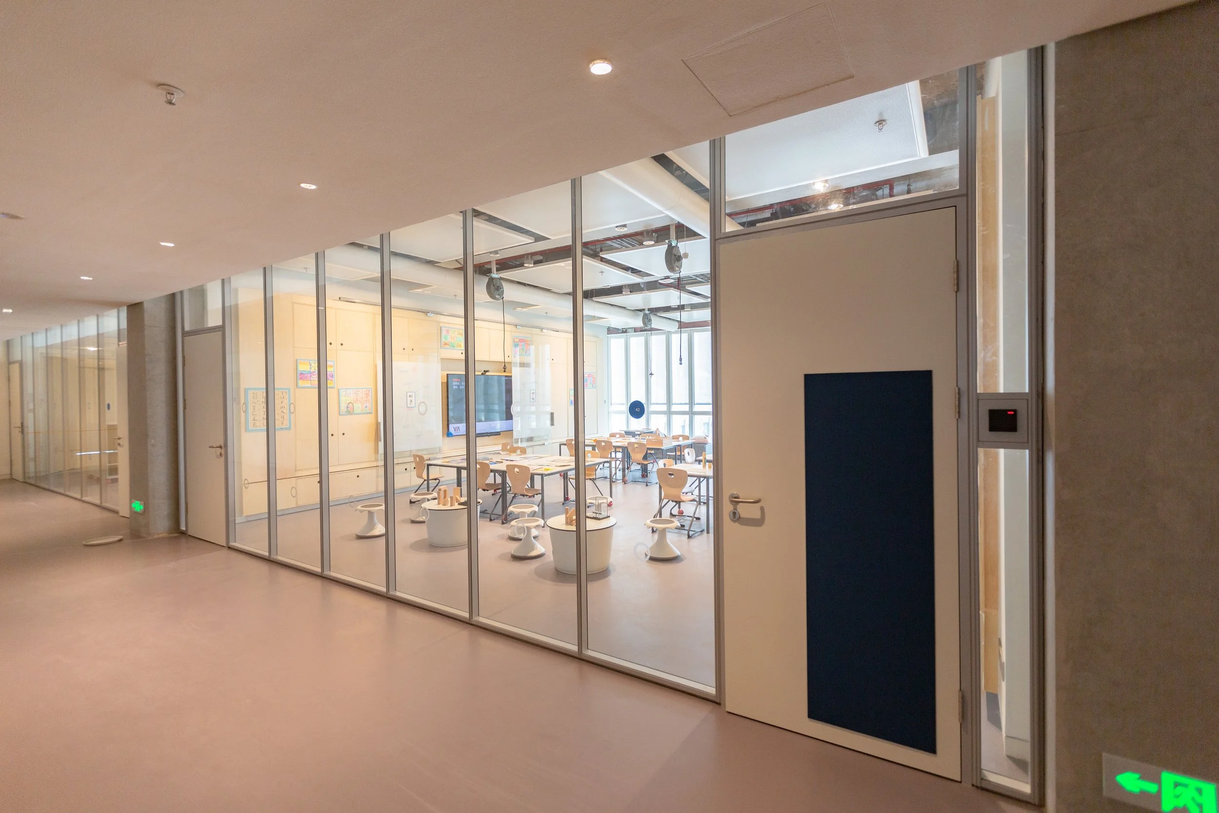 View from corridor revealing multiple classrooms with glass walls allowing views into classroom,