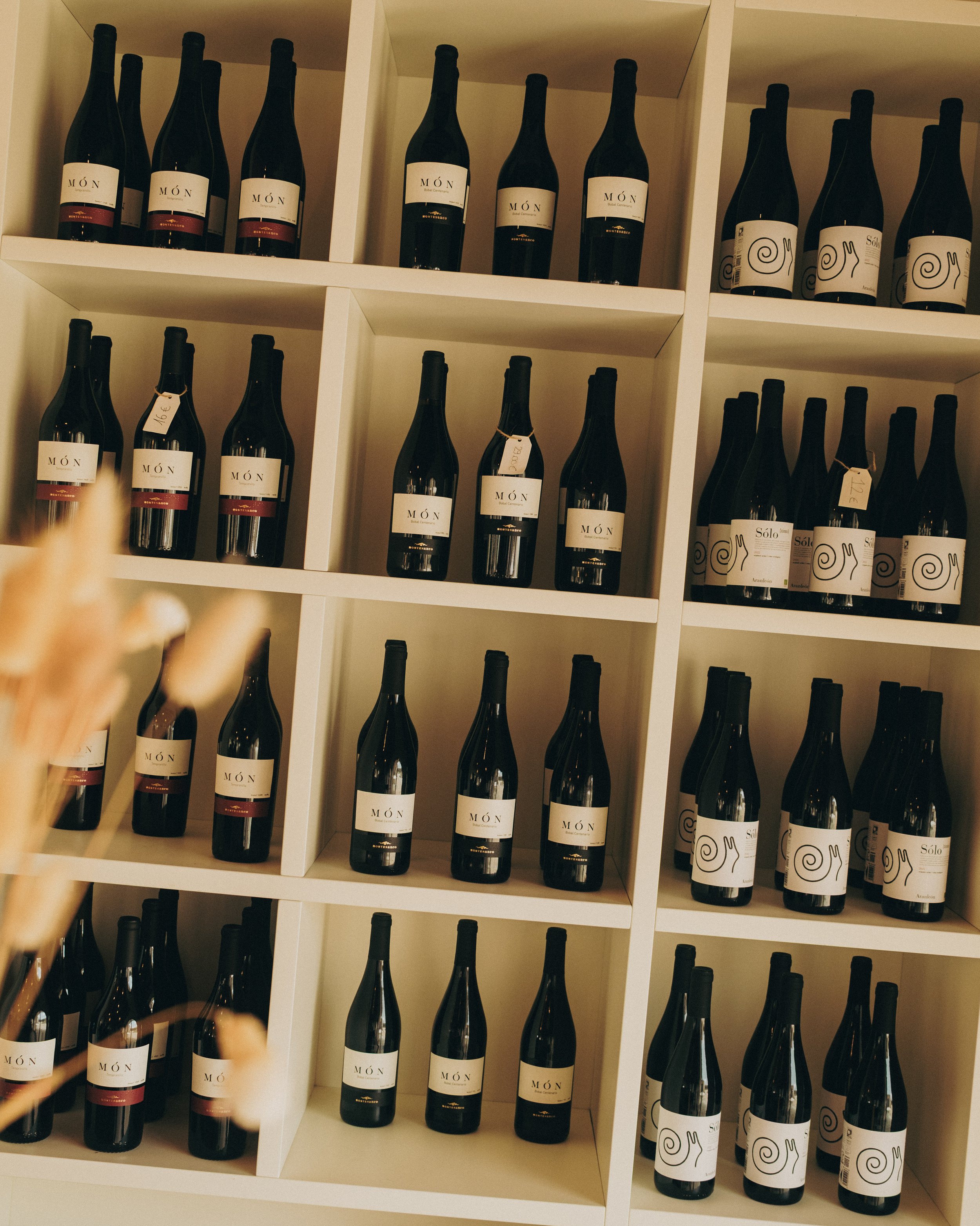 A wine rack with multiple bottles of wine arranged in cubbies, featuring black bottles with white labels and some with a design resembling a snail shell.